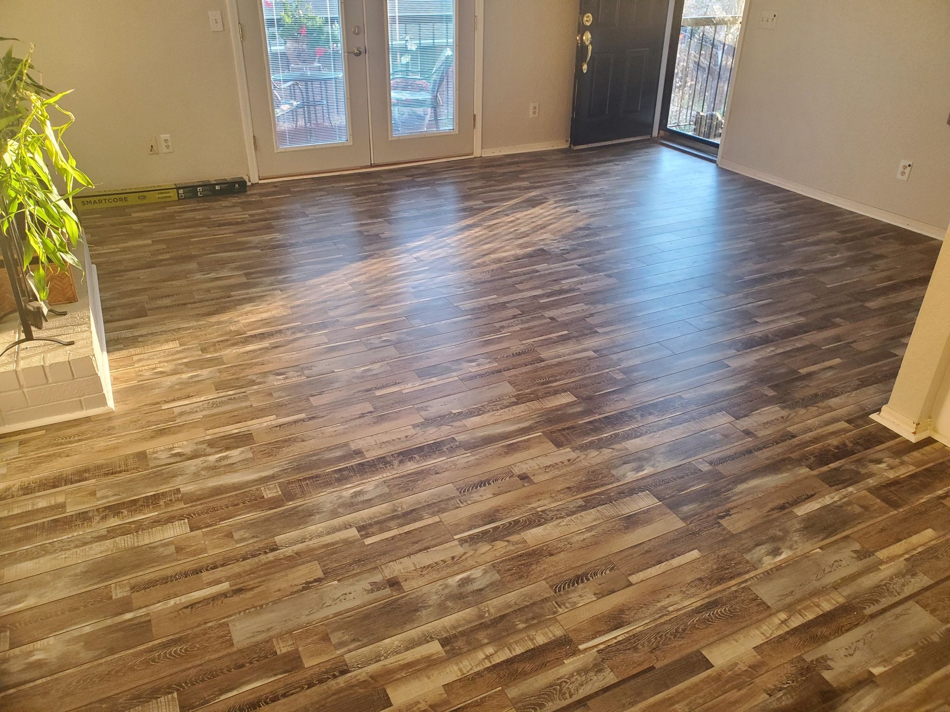 Empty room with brown wood-look flooring, beige walls, and sunlight from glass doors.