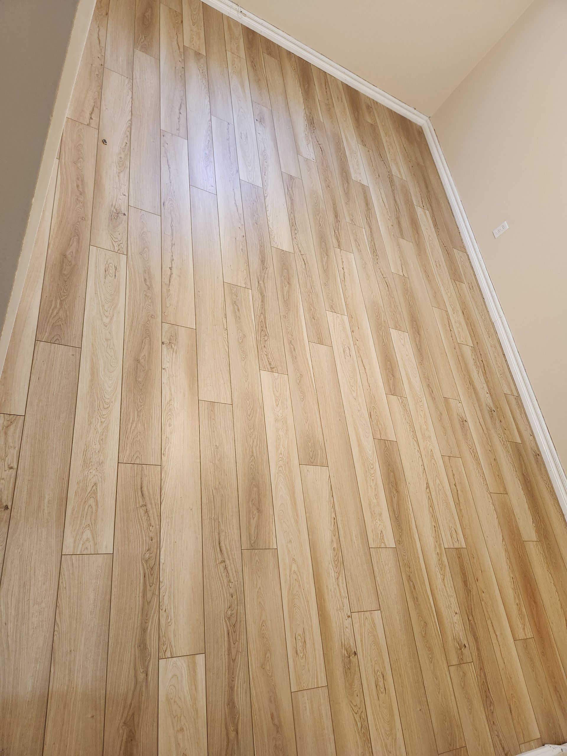 Empty room with light wood flooring and beige walls, viewed from a low angle.