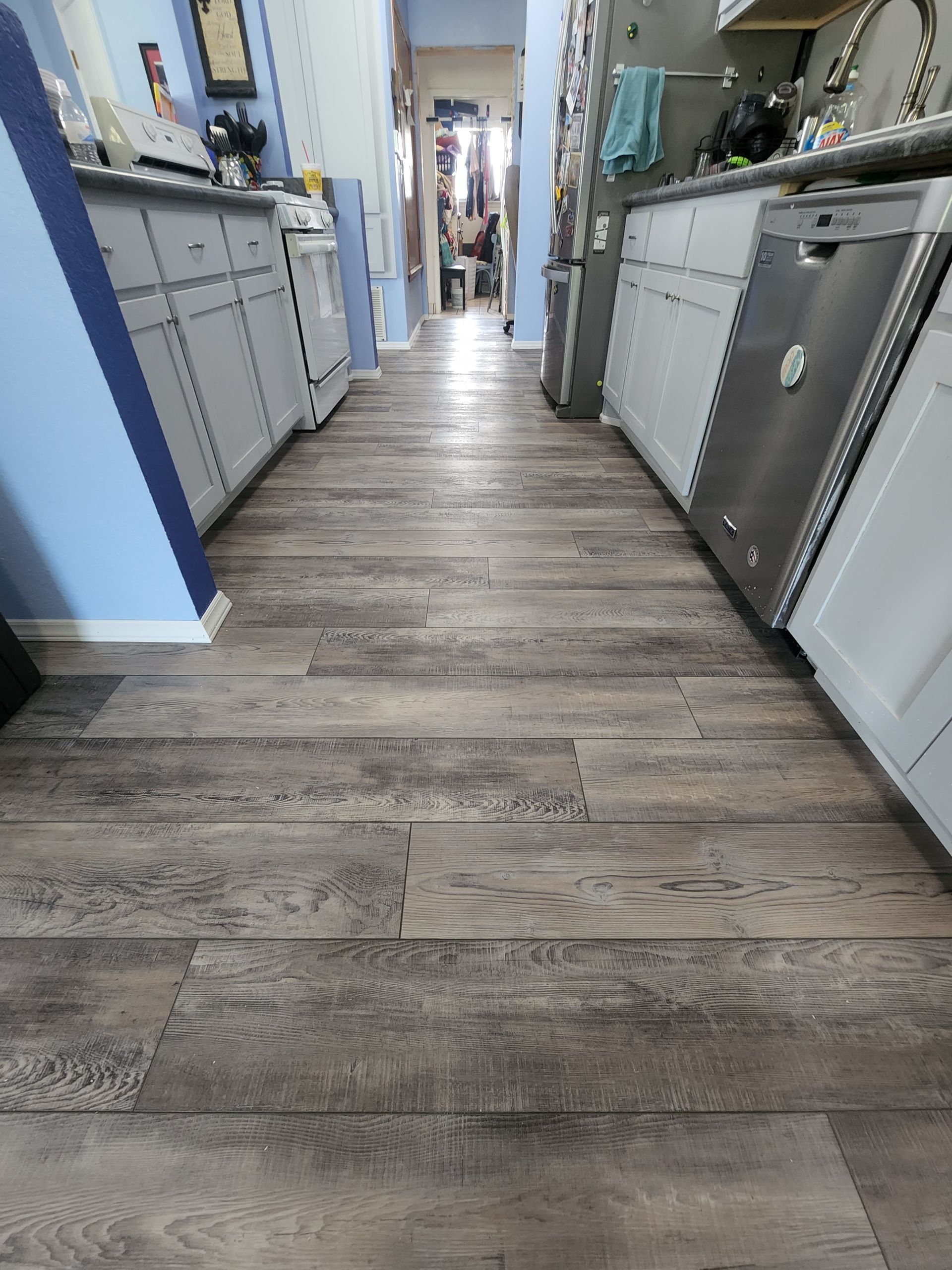 Narrow kitchen hallway with wood-look flooring and white cabinets on both sides