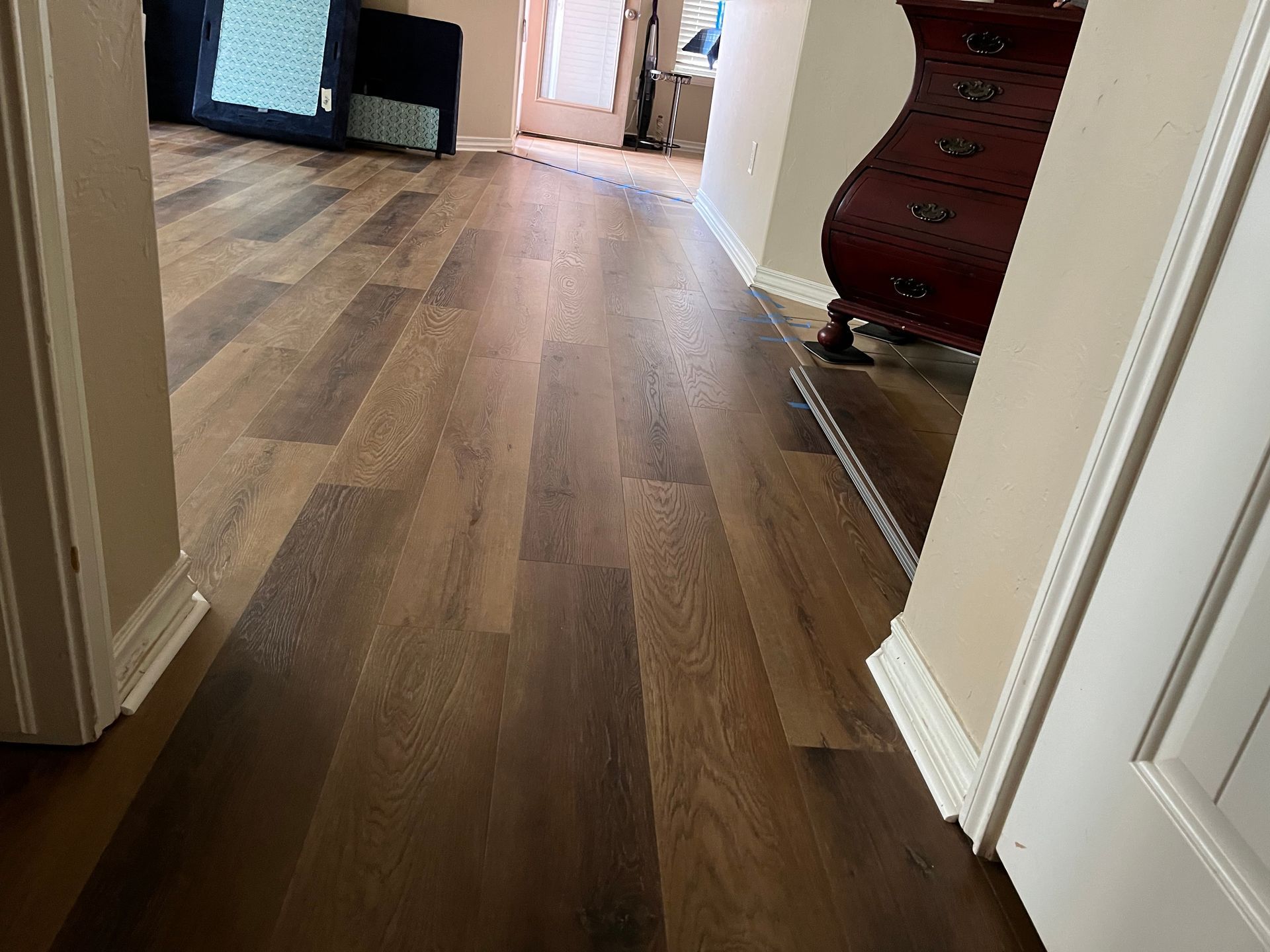 Wooden hallway floor leading to a doorway, with a dresser and TV stand in the distance.