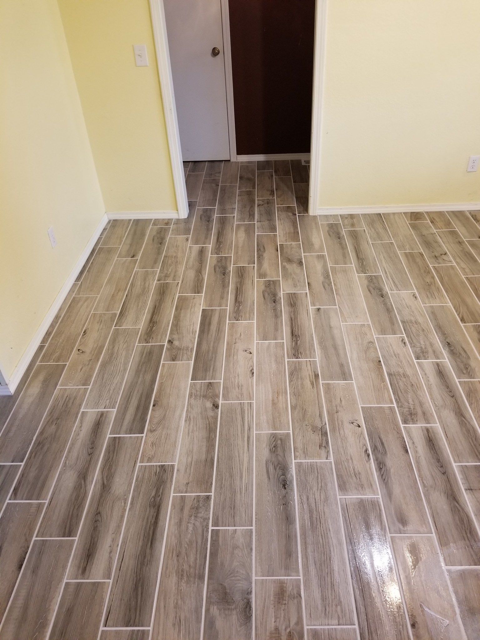 Empty tiled hallway with beige walls and a doorway in the back.