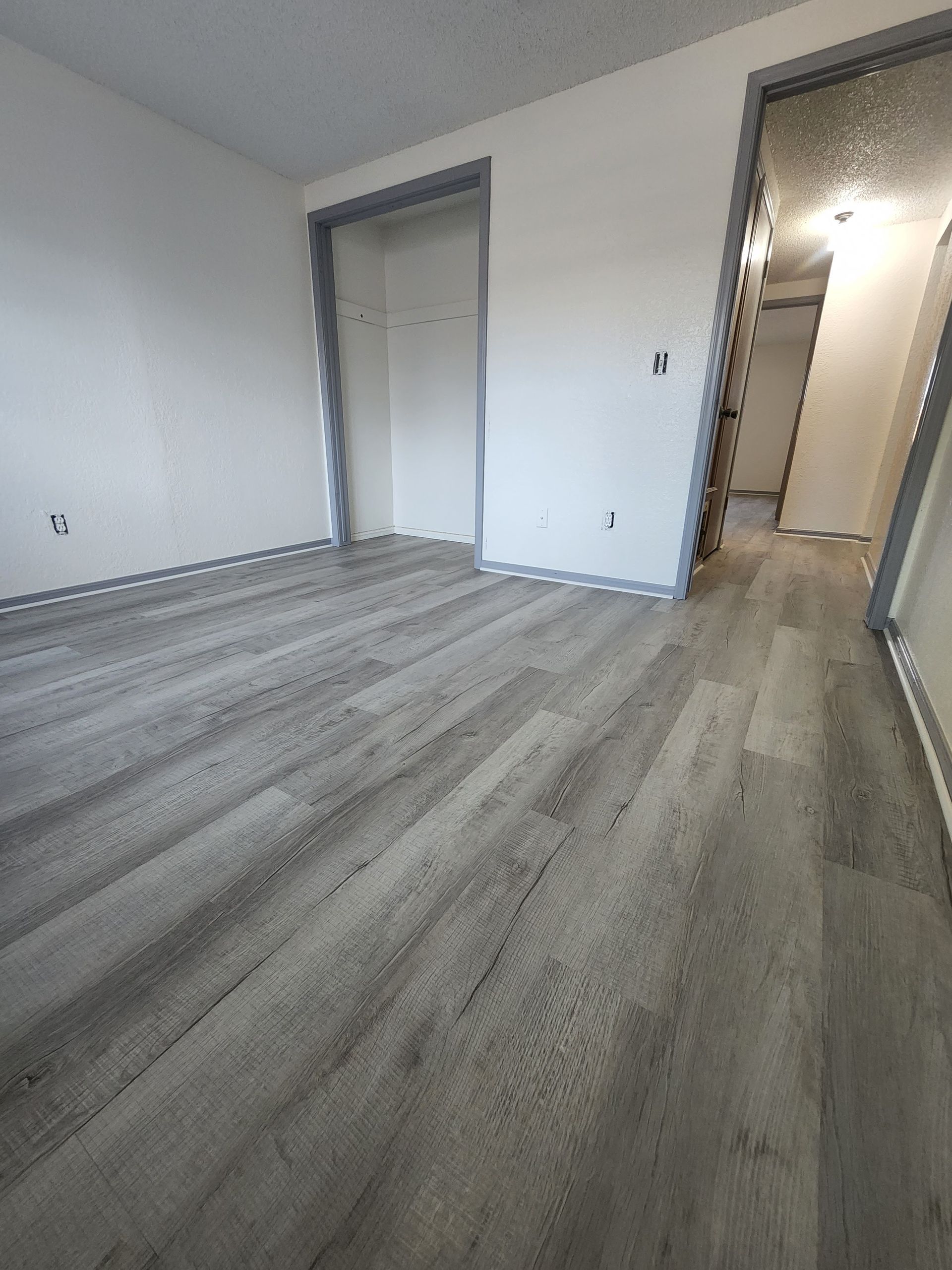 Empty room with light gray wood flooring, white walls, and an open doorway to a hallway