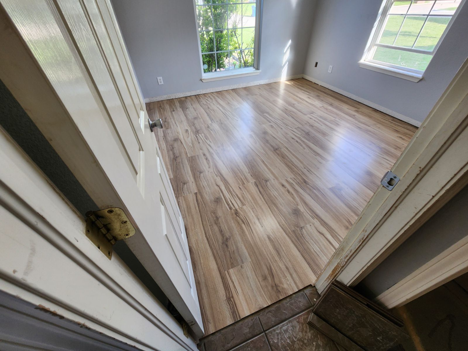 Empty room with light wood floors and white walls, viewed through an open doorway.