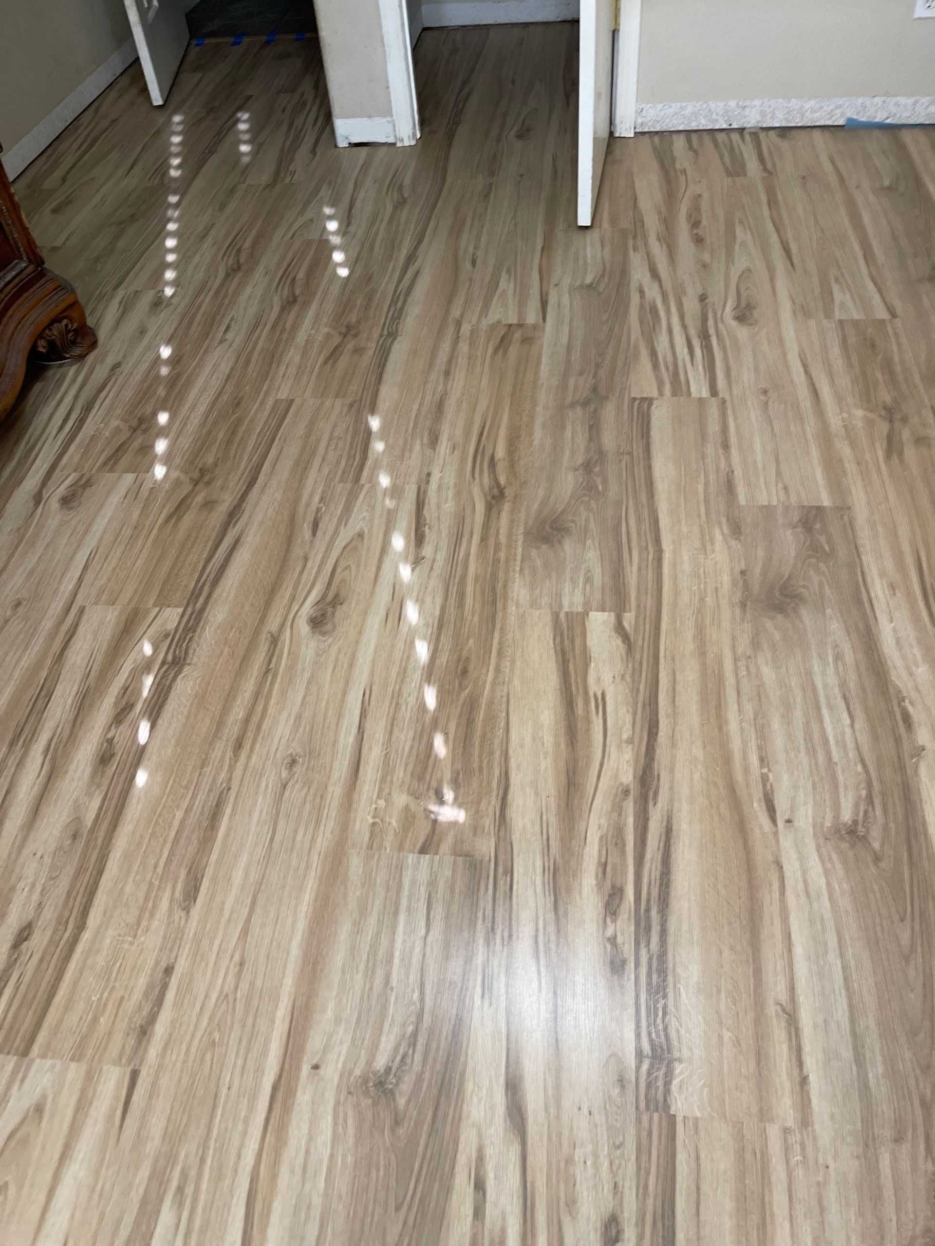Wood-look laminate floor with a line of white markers leading toward a doorway