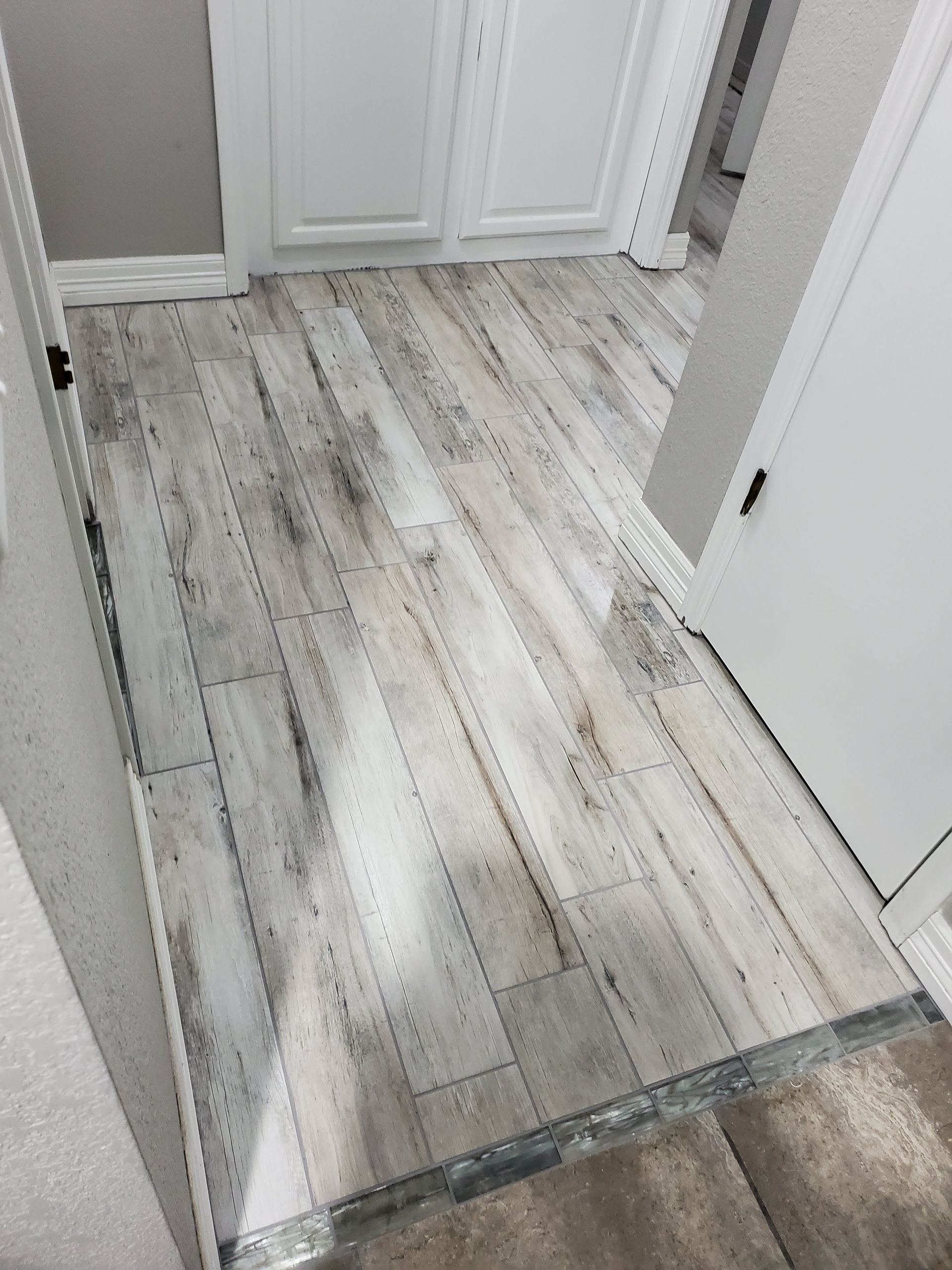 Light wood-look flooring in a hallway with white doors and baseboards