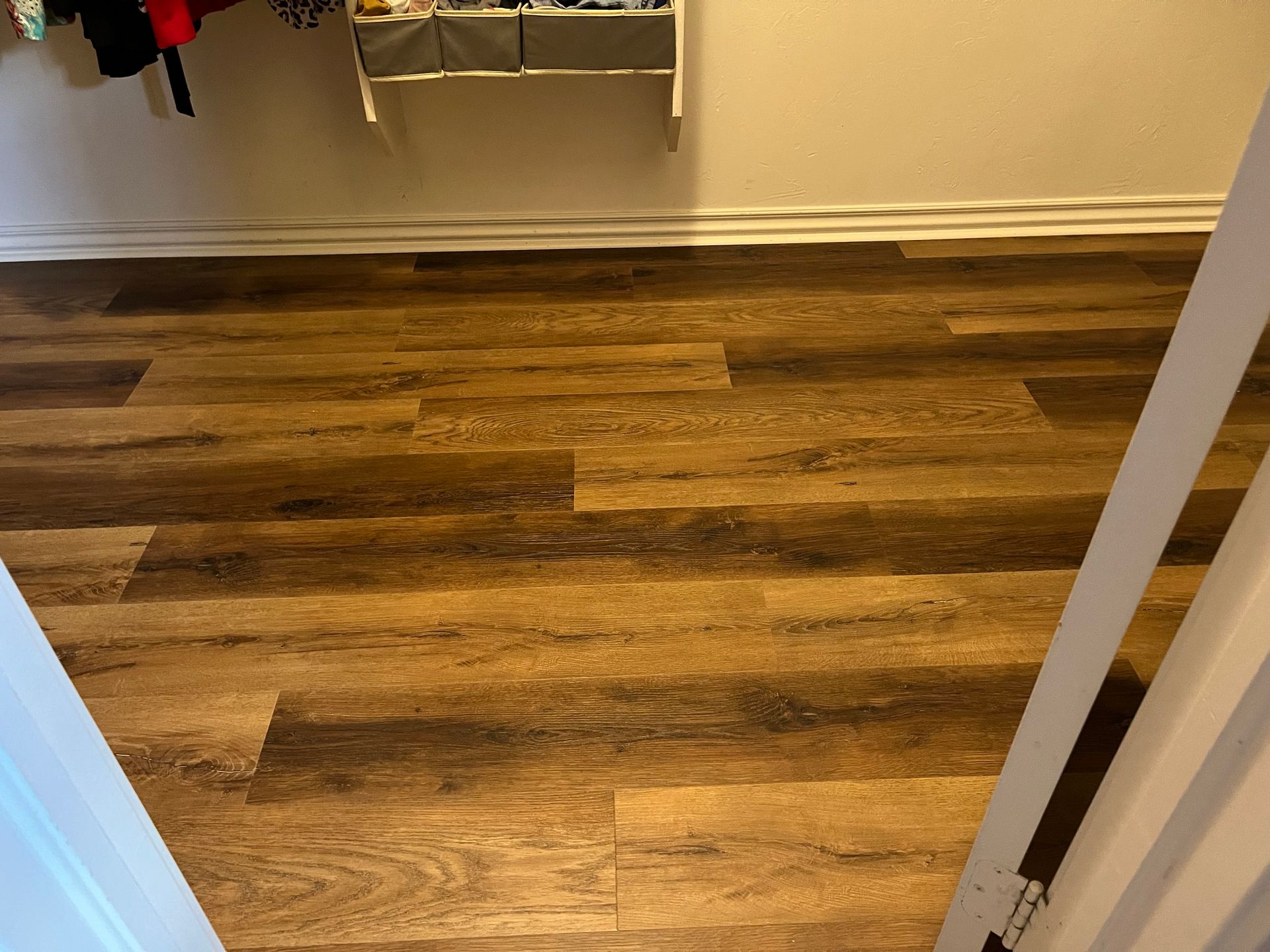 Wood-look laminate floor in a closet or hallway, with white walls and a hanging clothes rack visible.