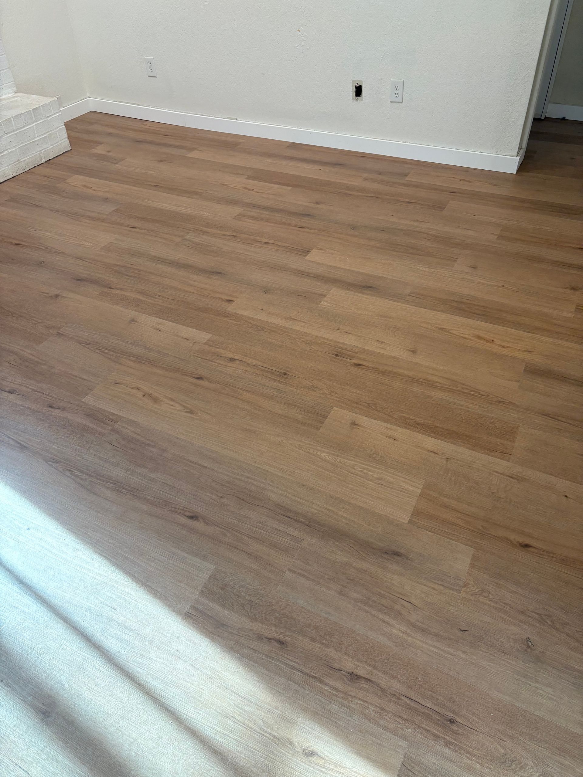 Empty room with light wood flooring, white walls, and sunlight streaming in from the left.
