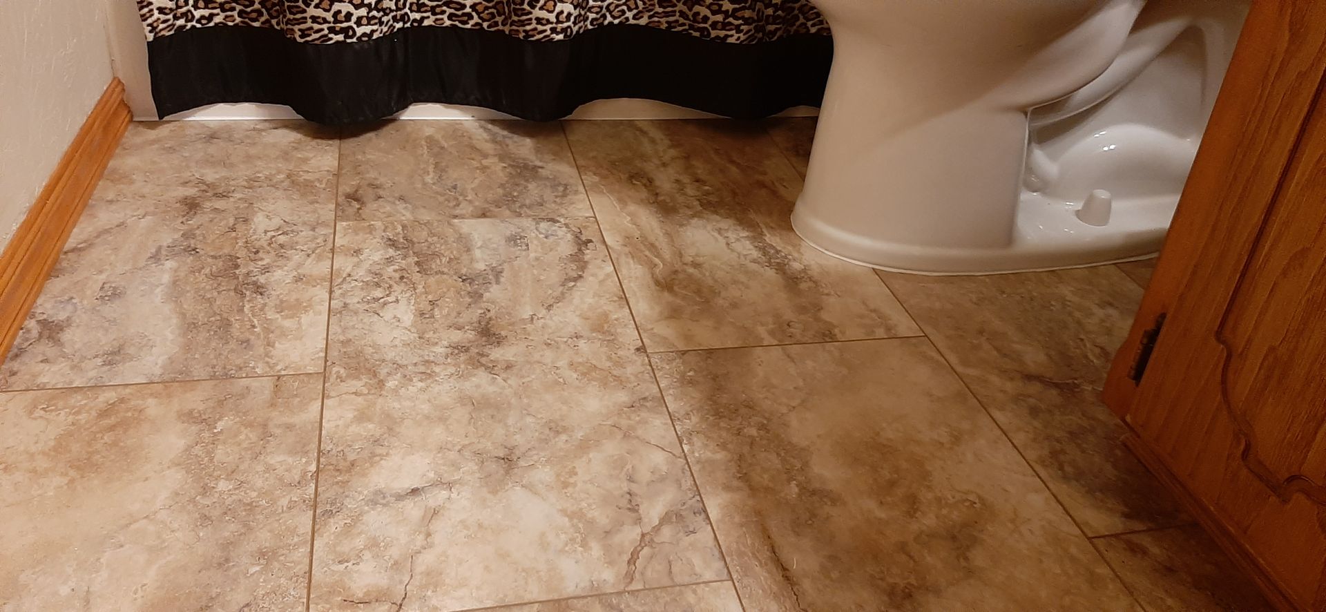 Bathroom floor with beige tile, dark shower curtain, toilet, and wooden cabinet