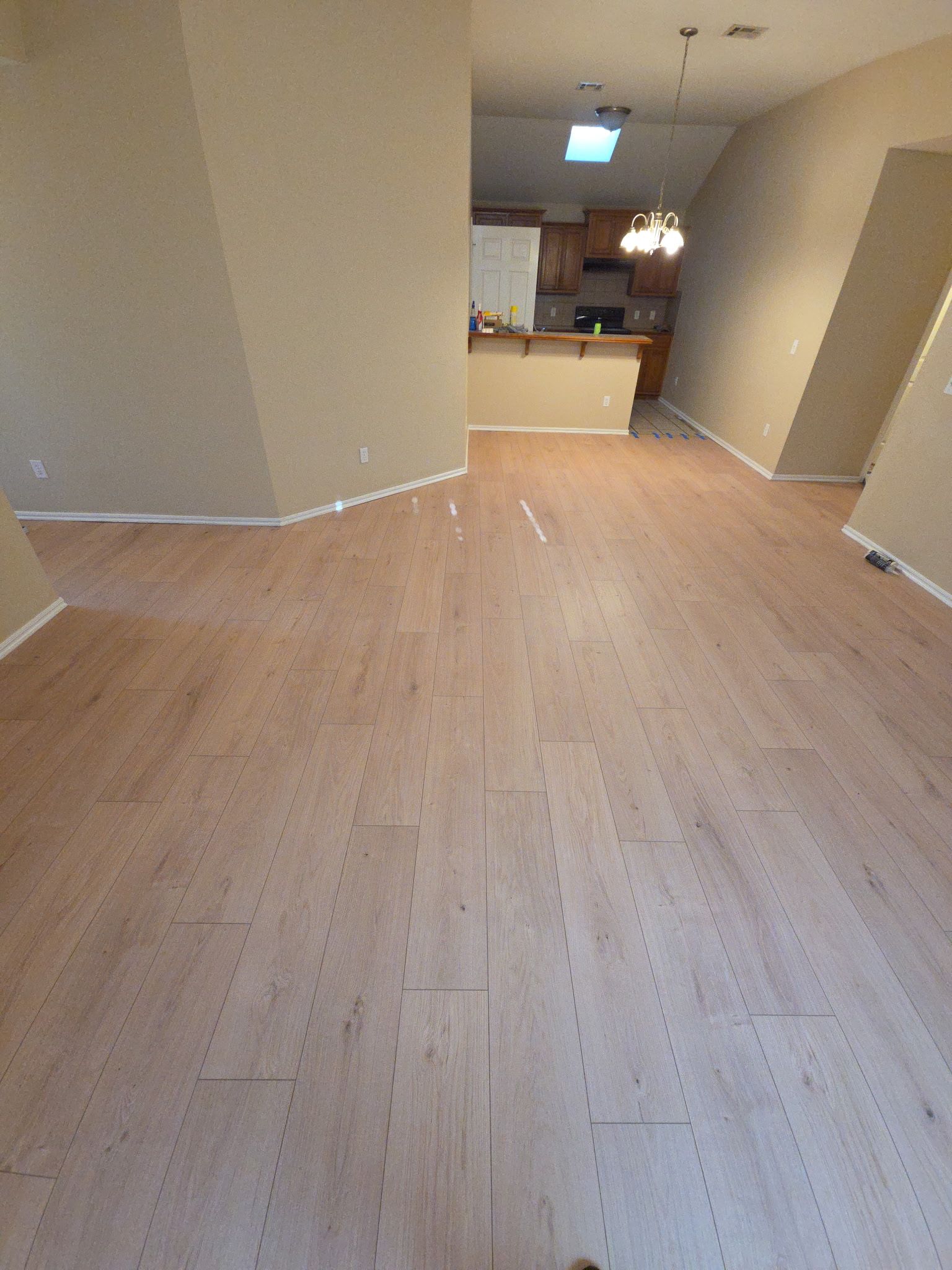 Empty hallway with light wood floor leading to a kitchen area
