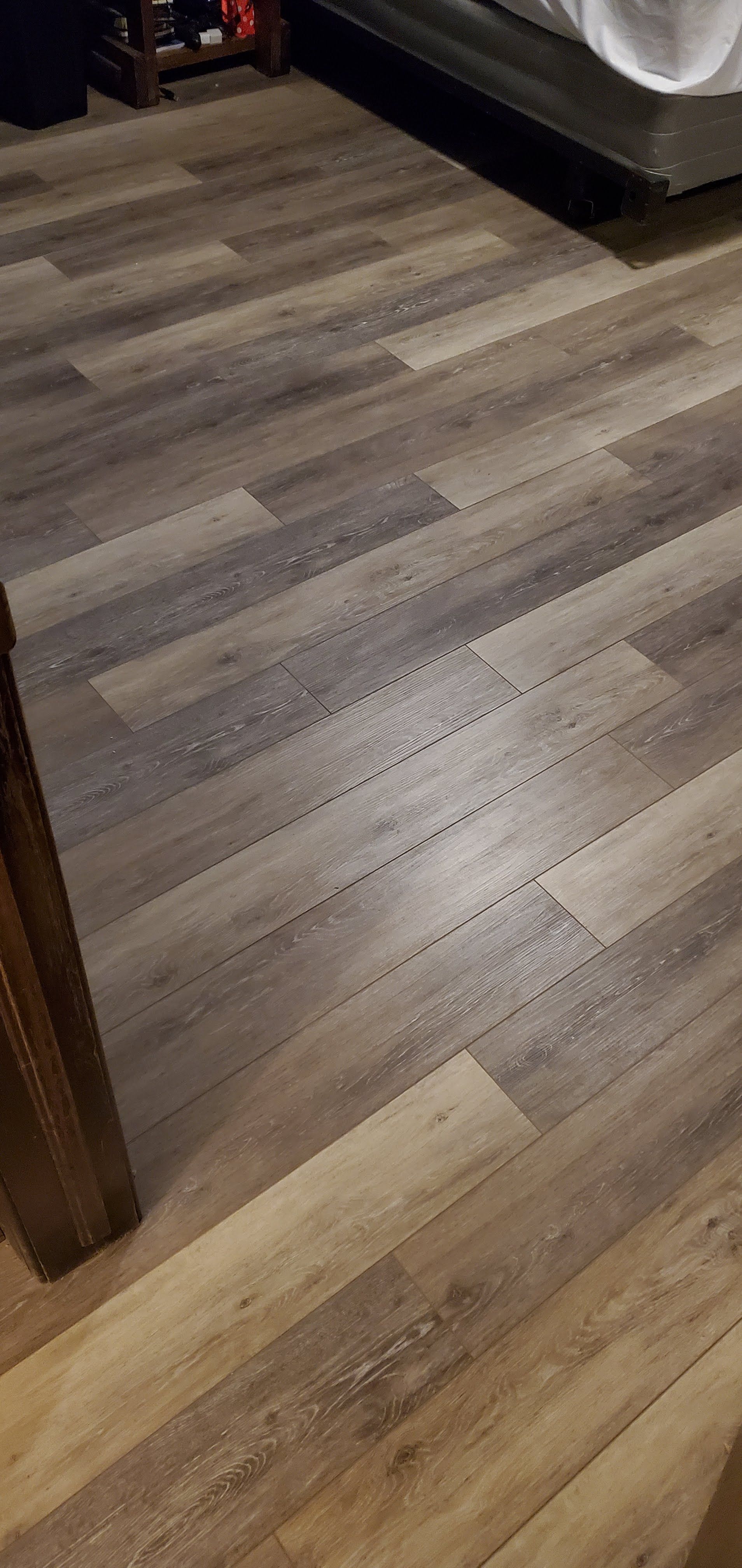 Wood-patterned laminate floor beside dark furniture and a bed frame