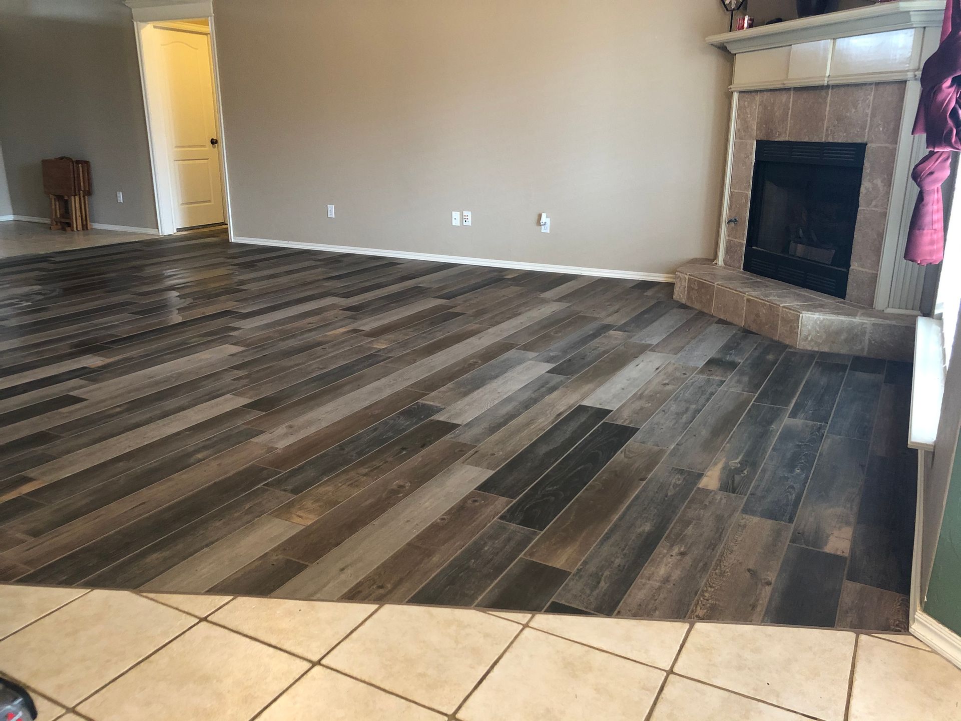 Empty living room with dark wood-look flooring, beige walls, and a fireplace.