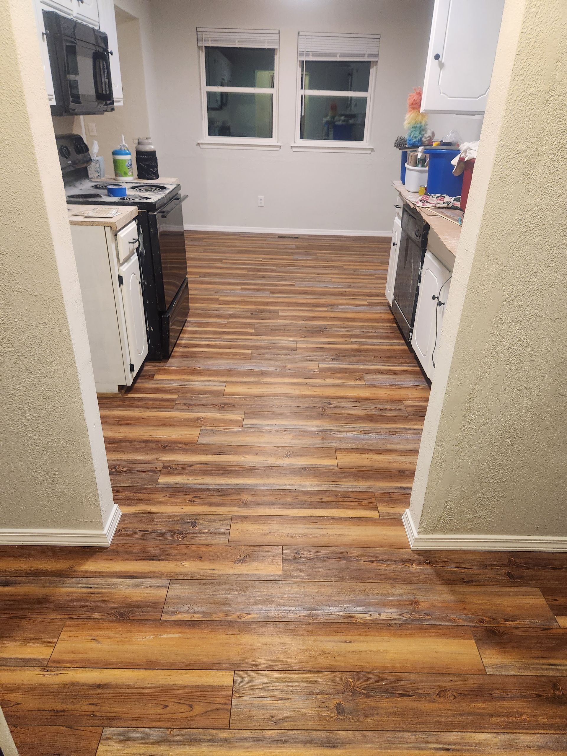 Narrow kitchen hallway with wood-look flooring, white cabinets, and a window at the far end.