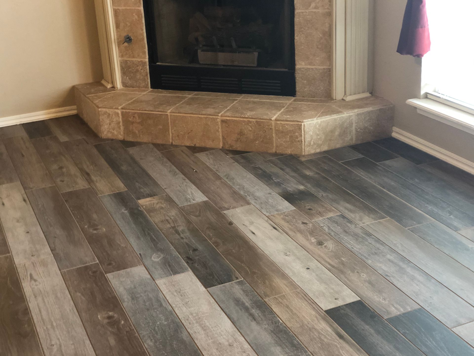 Wood-look plank flooring in a room with a stone fireplace and window seat.