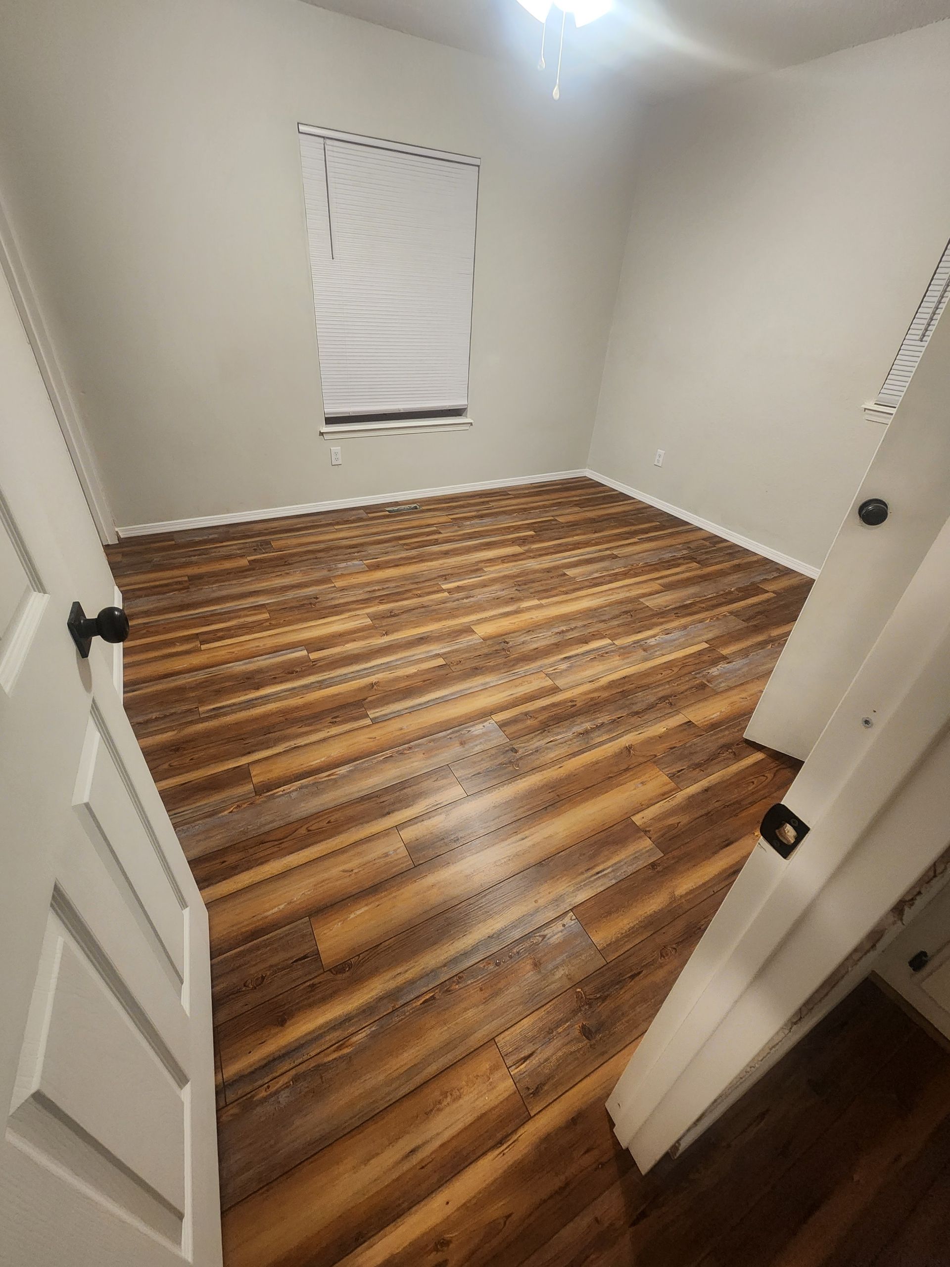 Empty room with wood floors, white walls, and a small window covered by a blind.