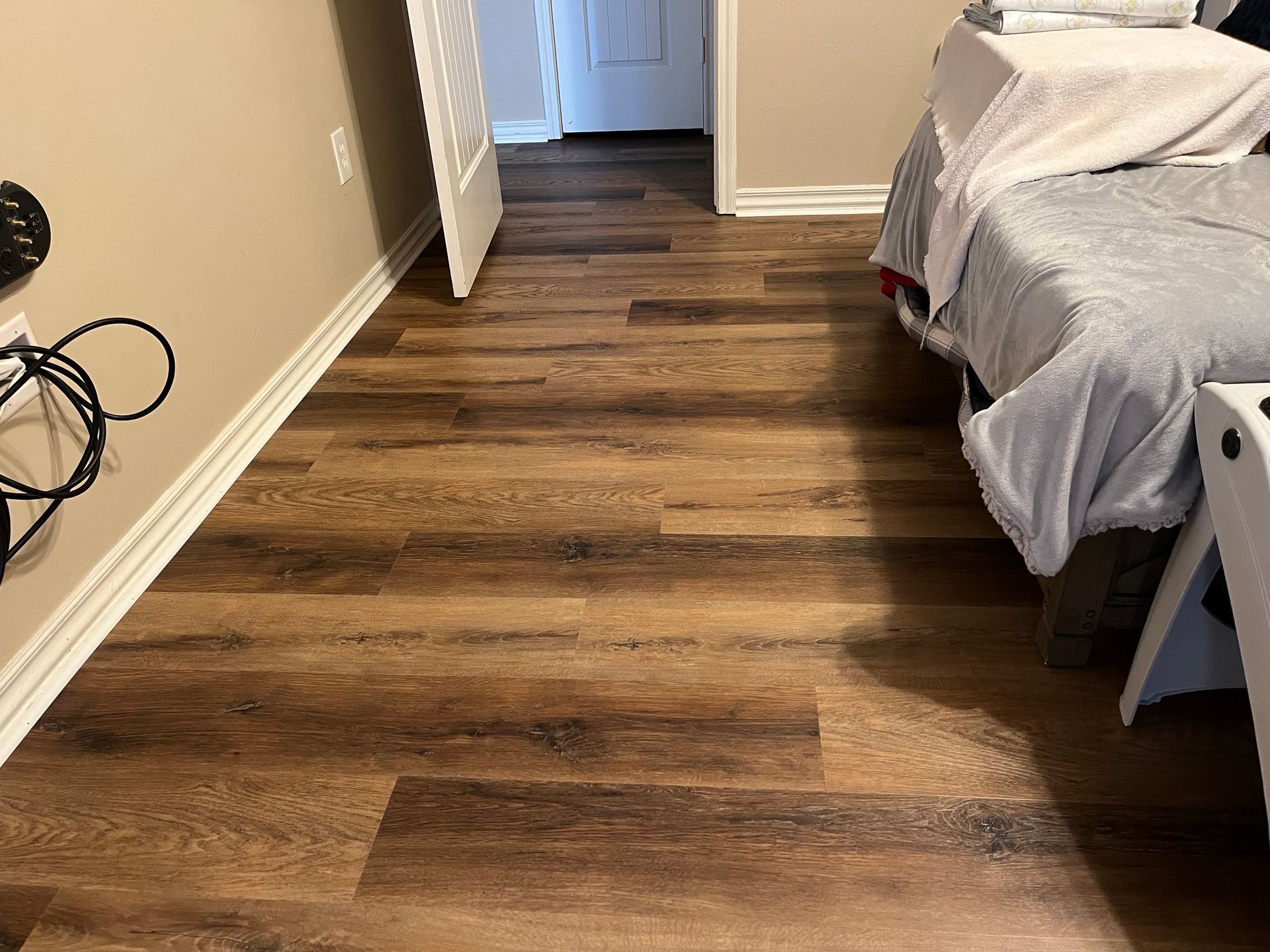 Empty bedroom with wood flooring, white walls, and a bed with gray bedding on the right.