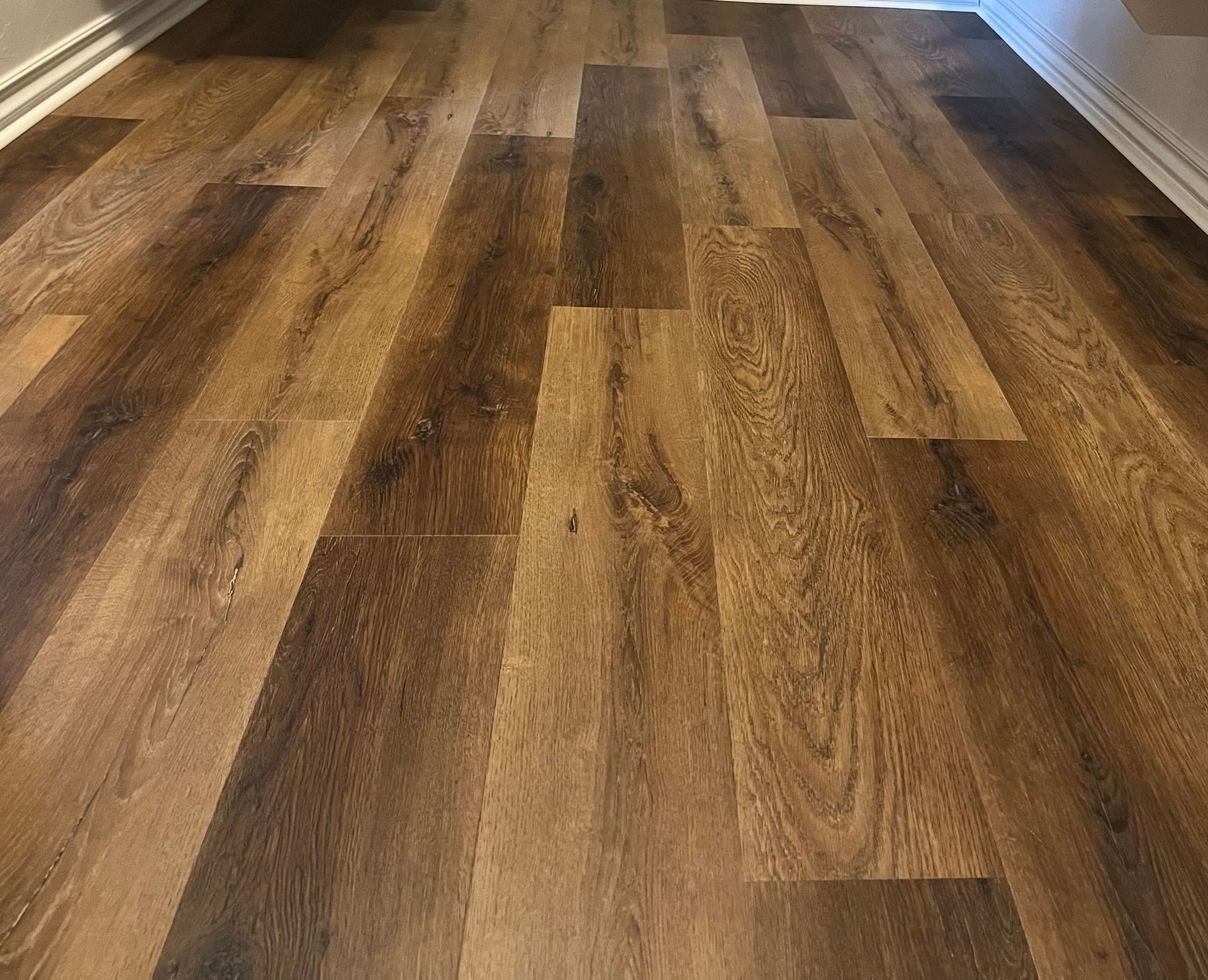 Wood-look plank flooring in warm brown tones, viewed down a hallway or room interior.