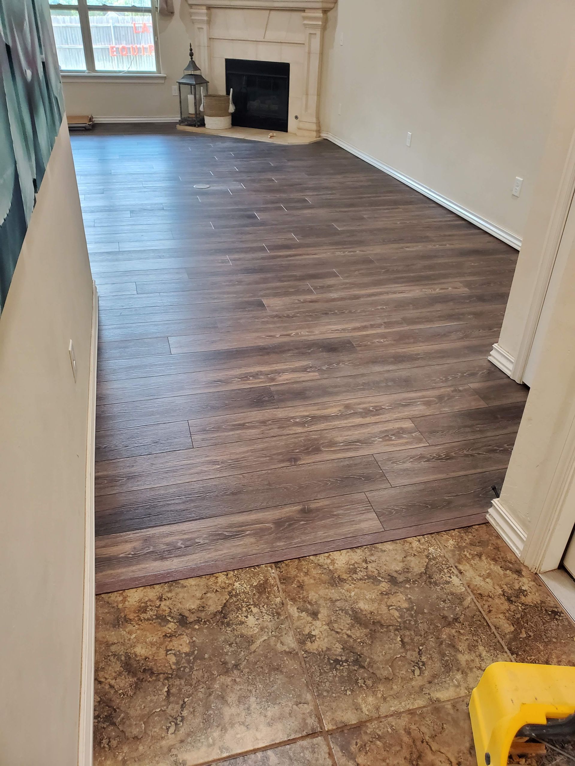Empty room with brown wood flooring, tan walls, and a fireplace at the far end.