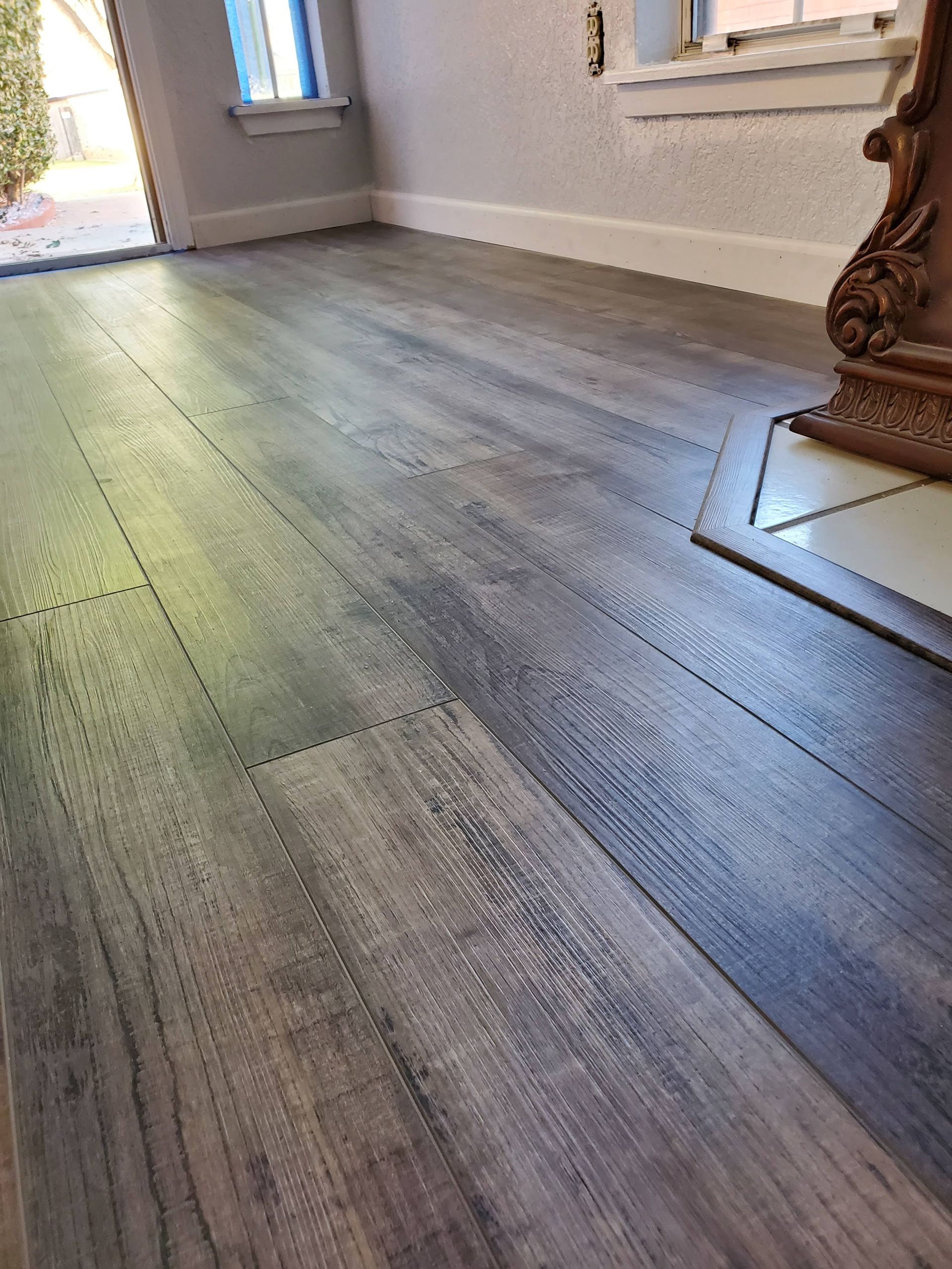 Wood-look gray plank flooring in a bright room with sunlight and a window visible