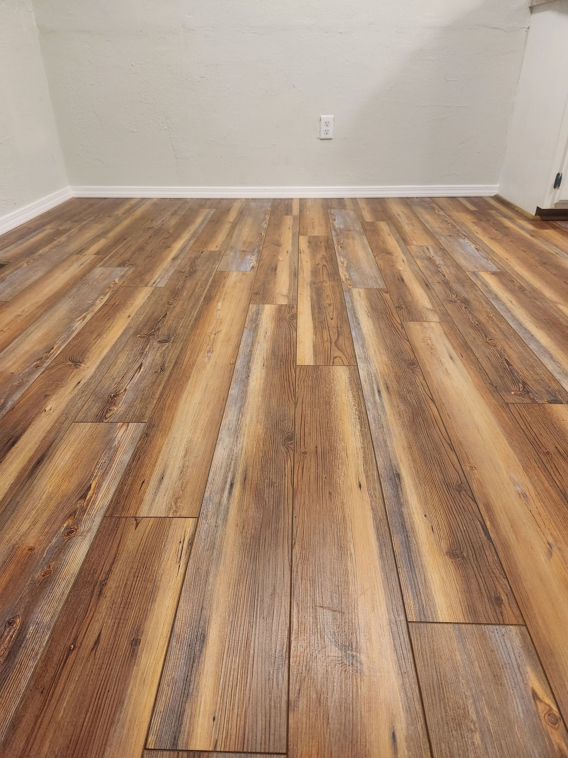 Empty room with wood-pattern vinyl flooring and white walls, viewed from floor level