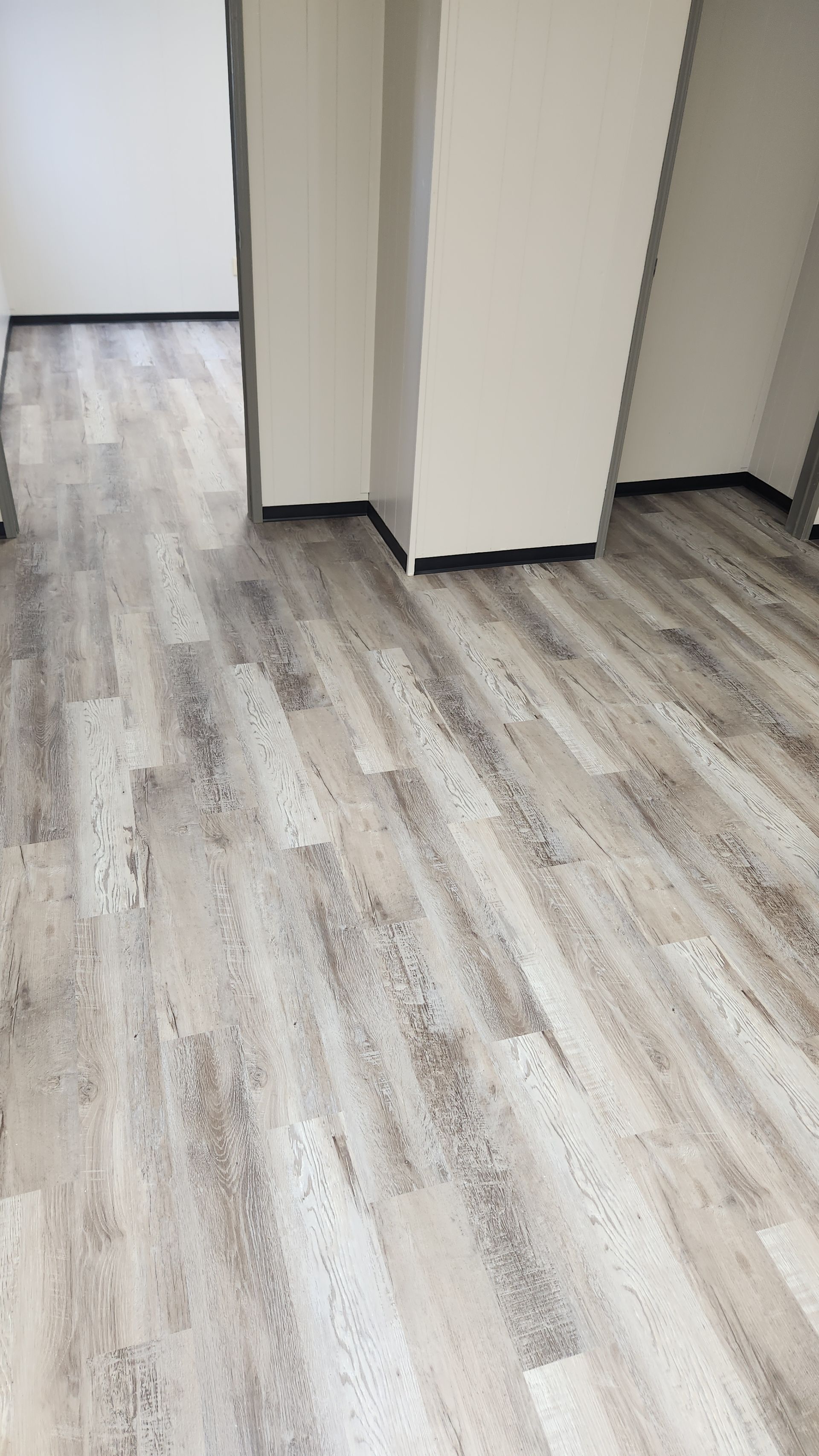 Empty hallway with light gray wood flooring and white walls.