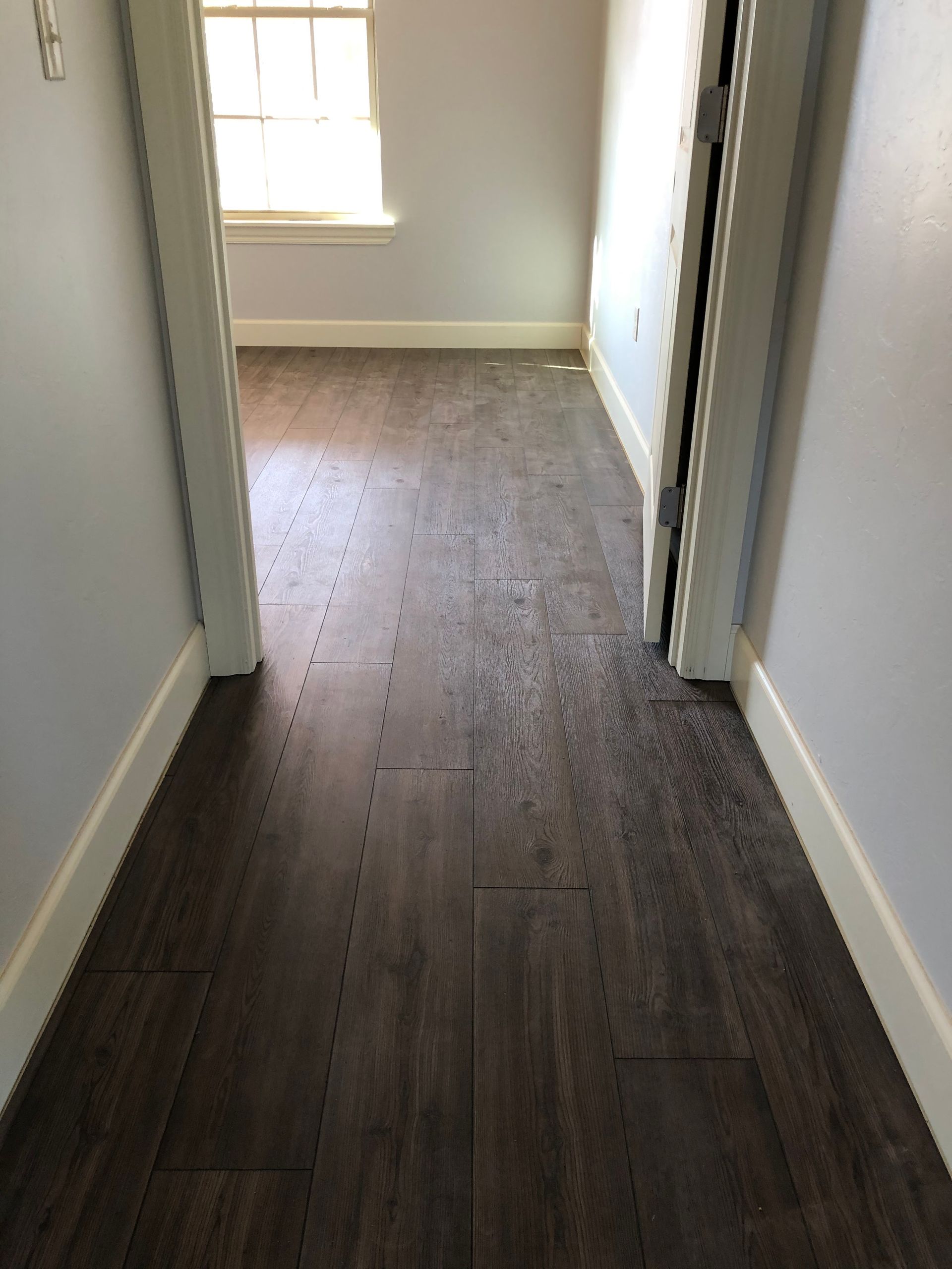 Narrow hallway with dark wood floors, white walls, and a window at the end.