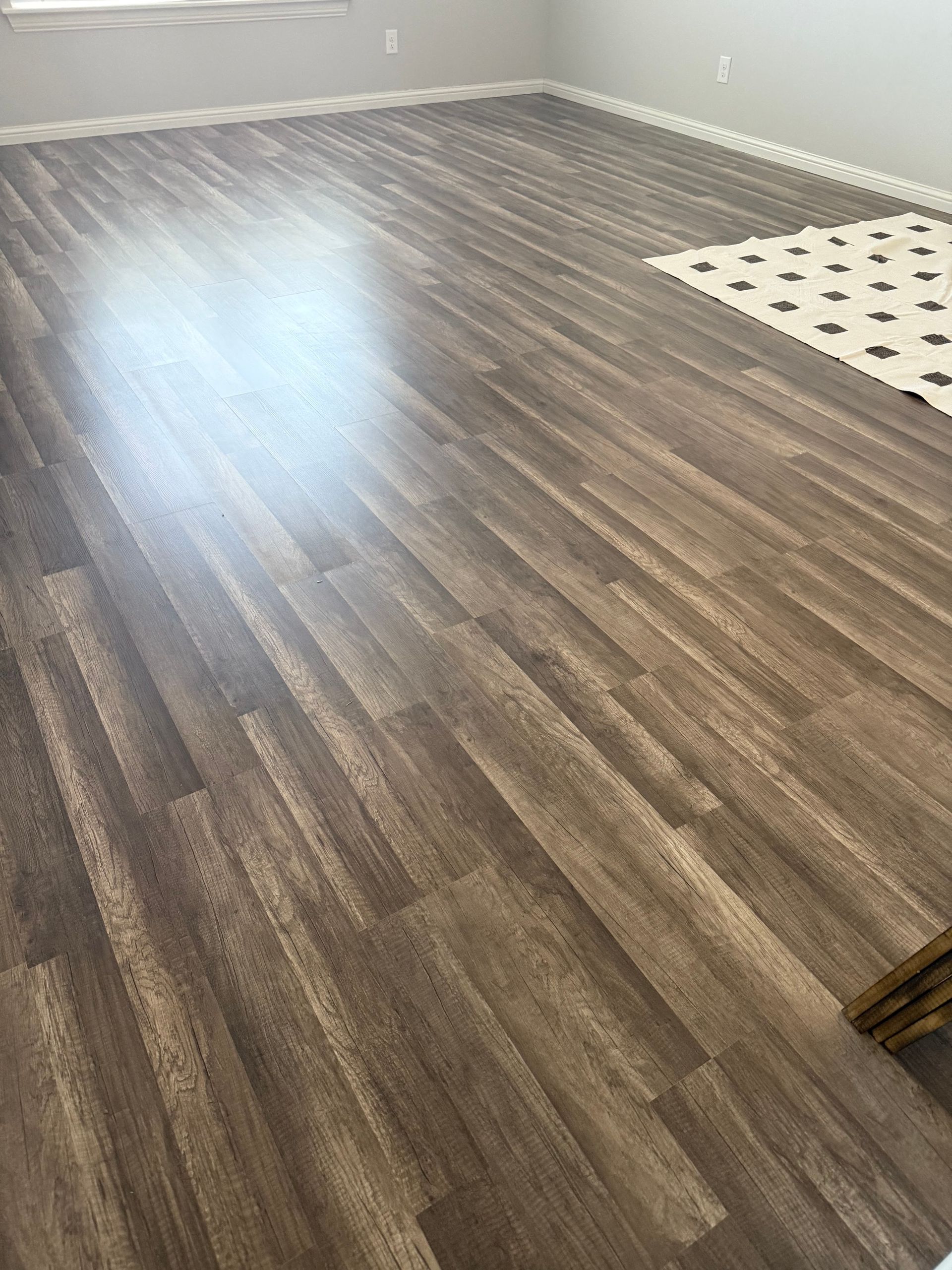 Empty room with gray-brown wood flooring and a white pet mat in the corner.