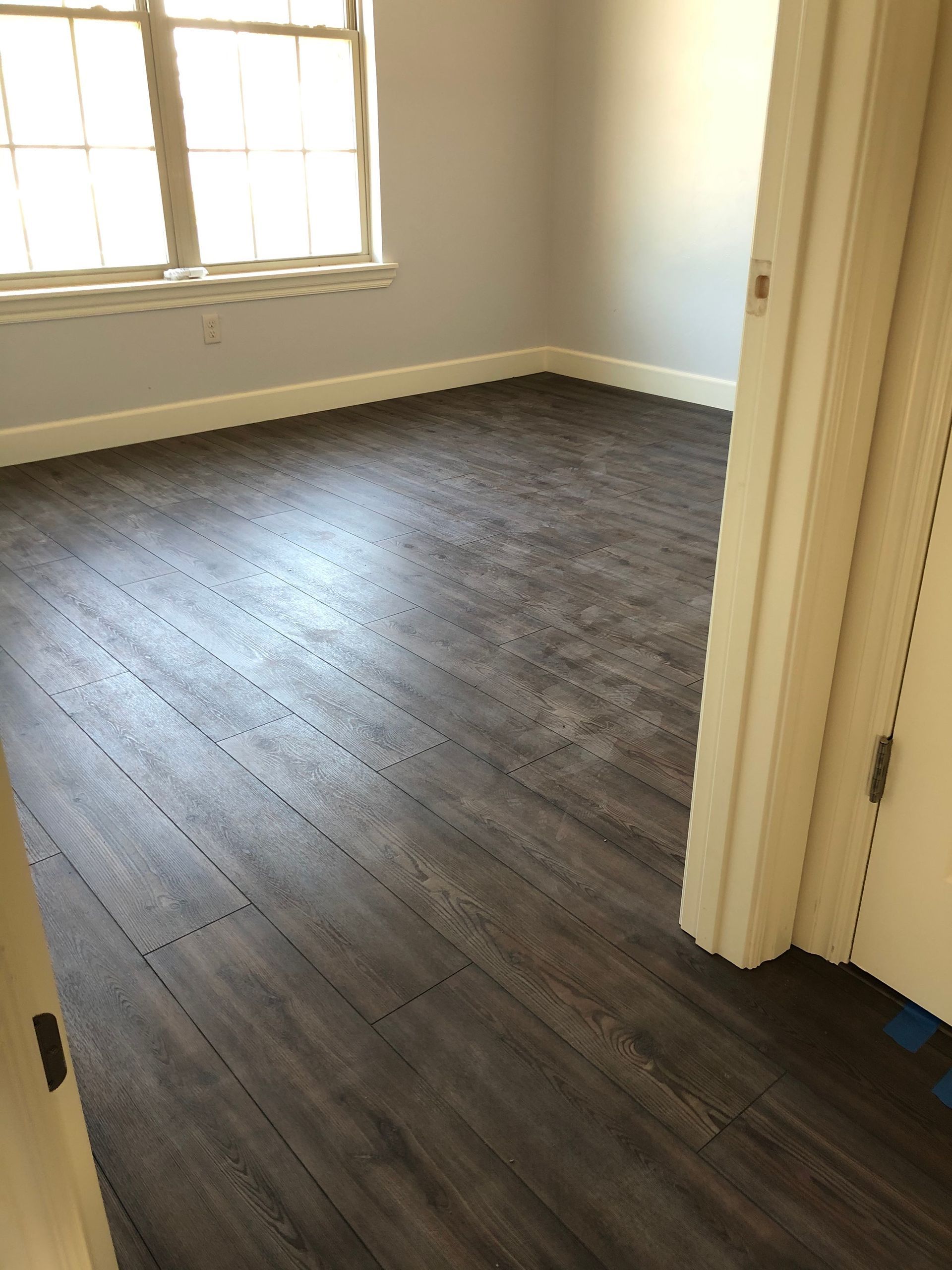 Empty room with dark wood floor, white walls, and sunlight from a window.