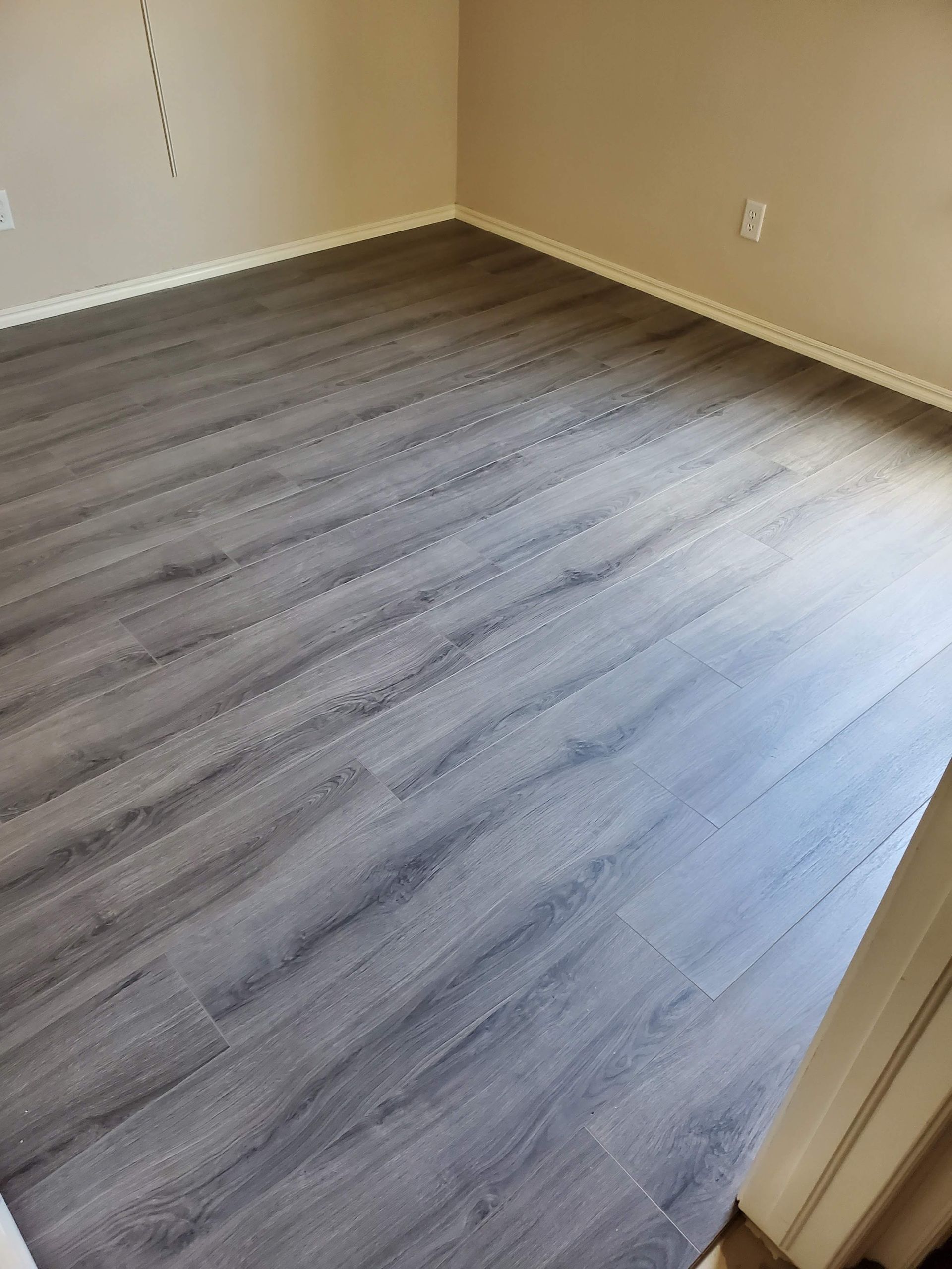 Empty room with gray wood-look flooring and beige walls, viewed from the doorway.