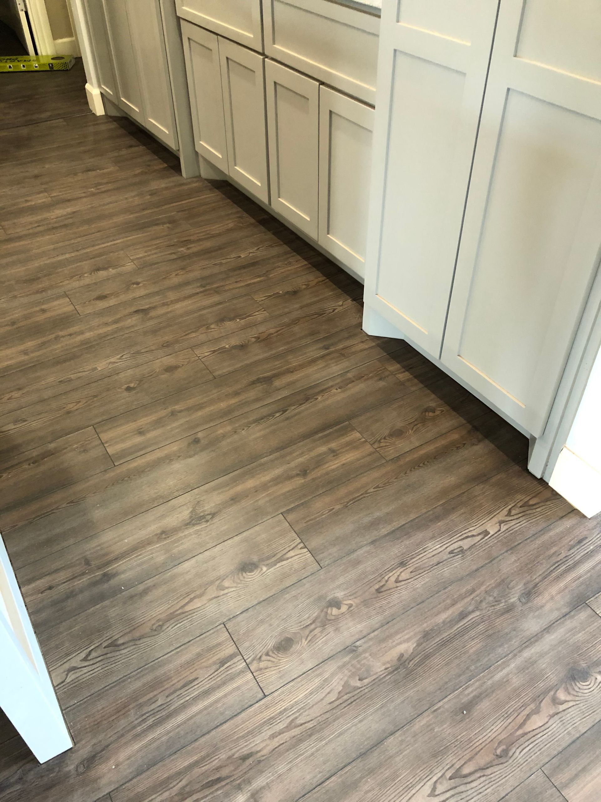 Narrow kitchen hallway with gray wood flooring and white cabinets along one side.