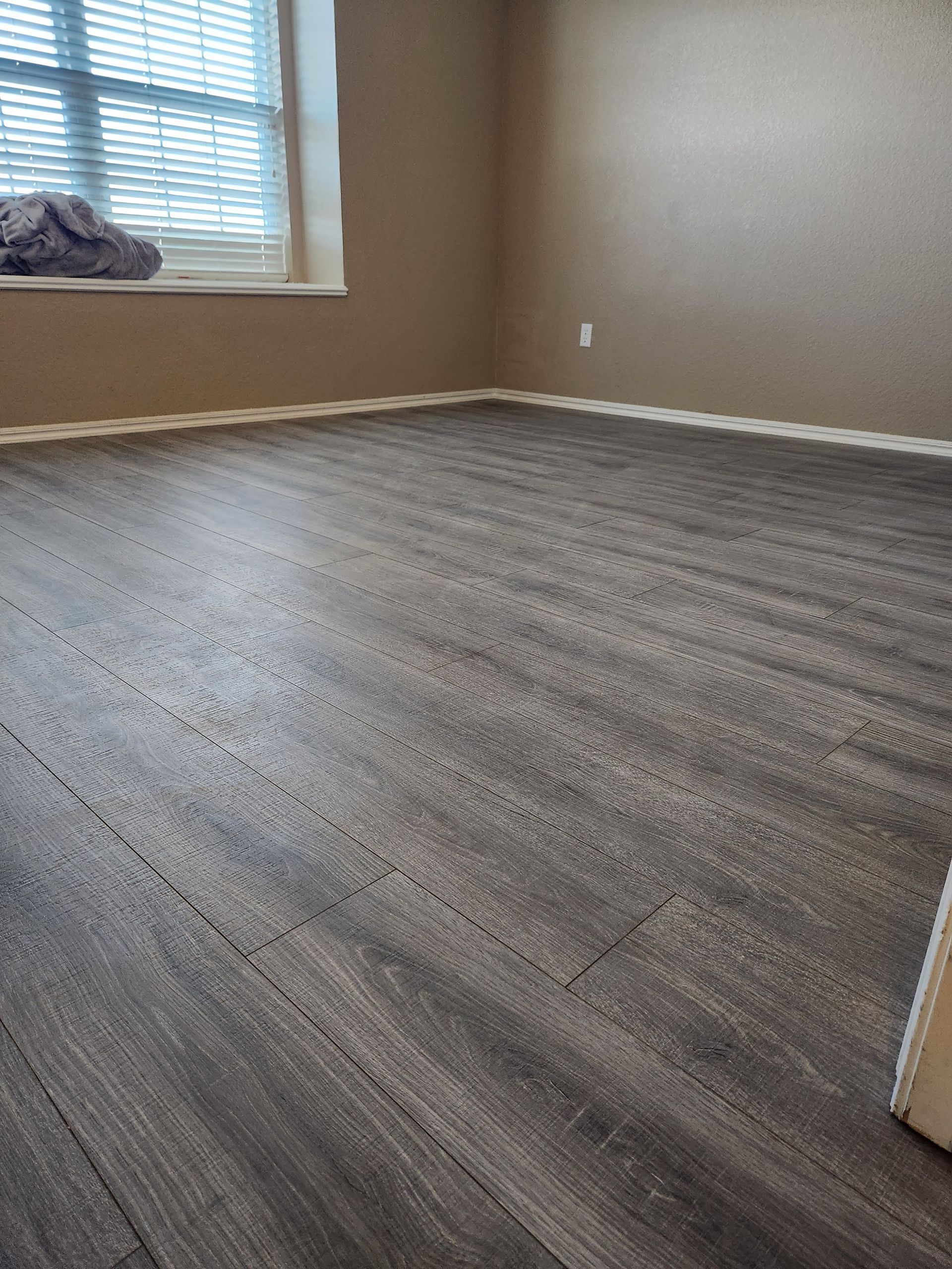 Empty room with gray wood-look flooring, beige walls, and a window letting in daylight