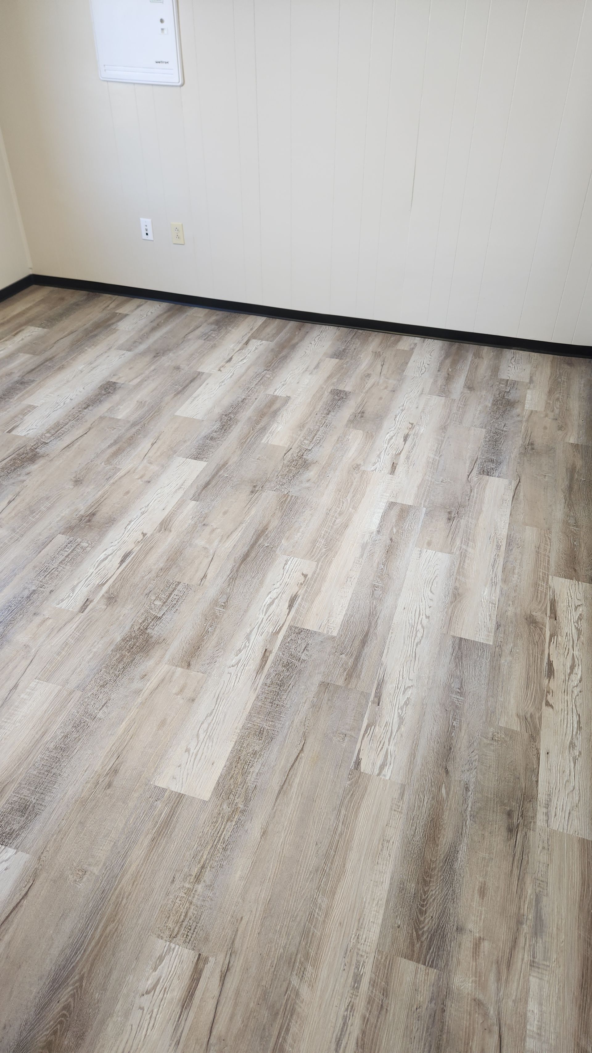 Empty room with light wood flooring, white walls, and a dark baseboard trim
