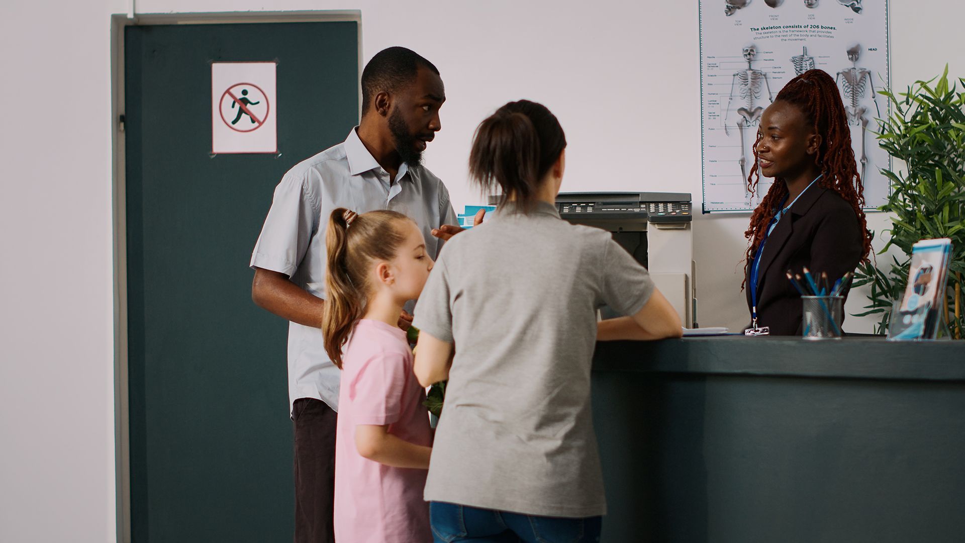 Family at a doctor's office reception desk; dark-skinned receptionist helping them.