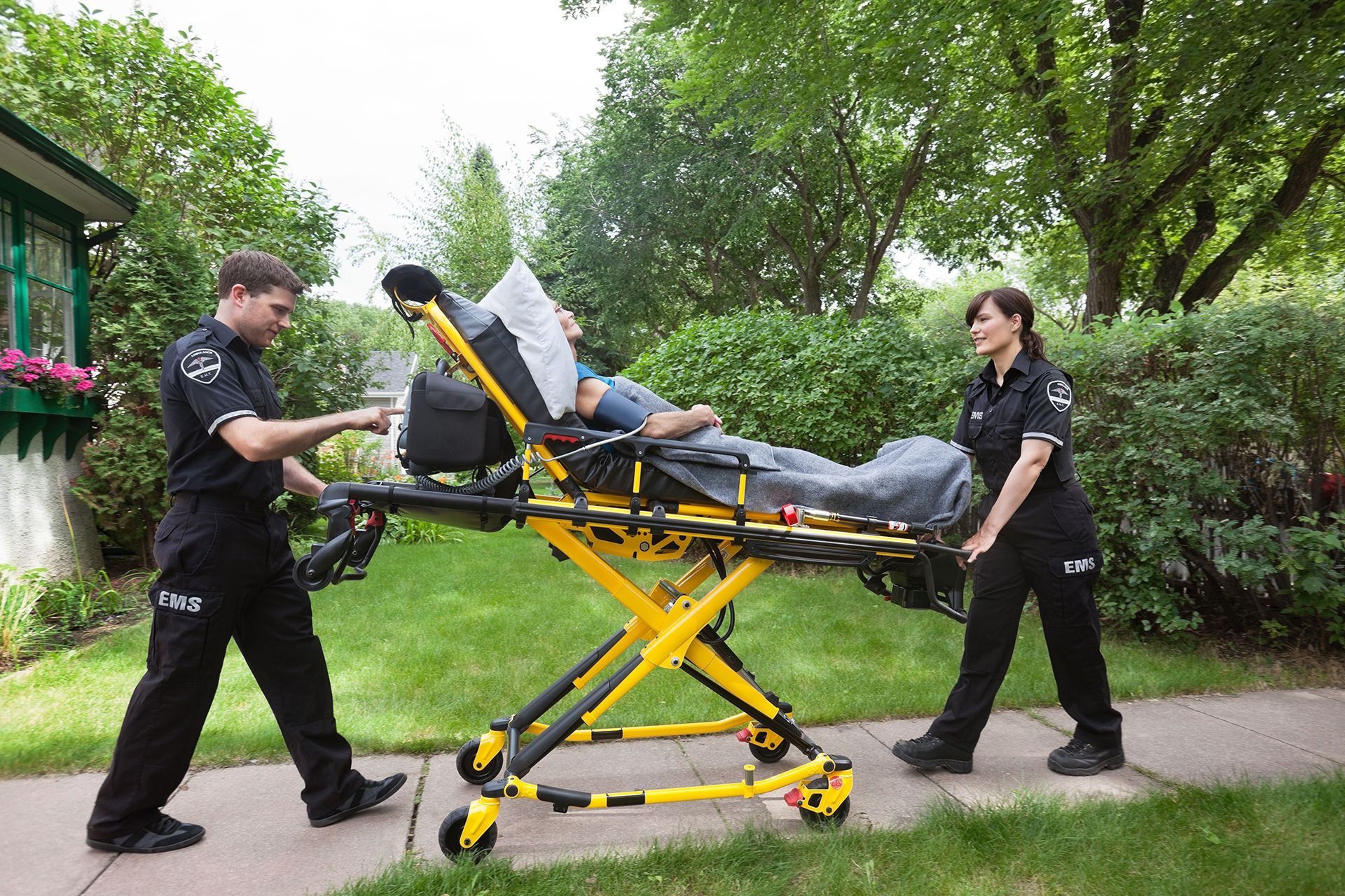Two paramedics transport a patient on a stretcher outdoors.