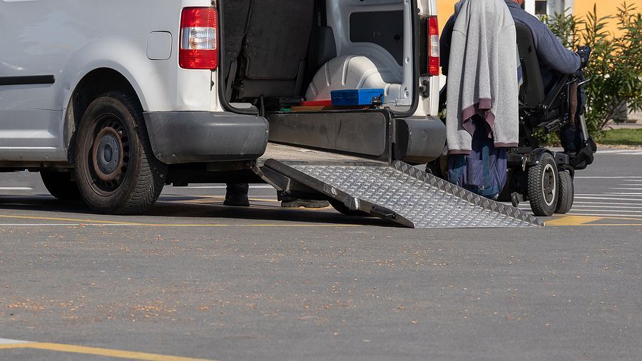 White van with a ramp extended, a person in a wheelchair prepares to enter the vehicle.