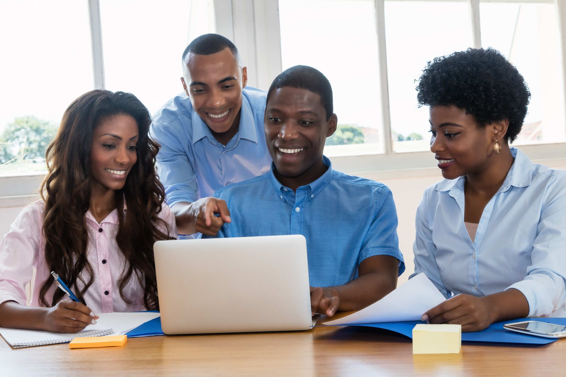a group of people are sitting around a table looking at a laptop computer