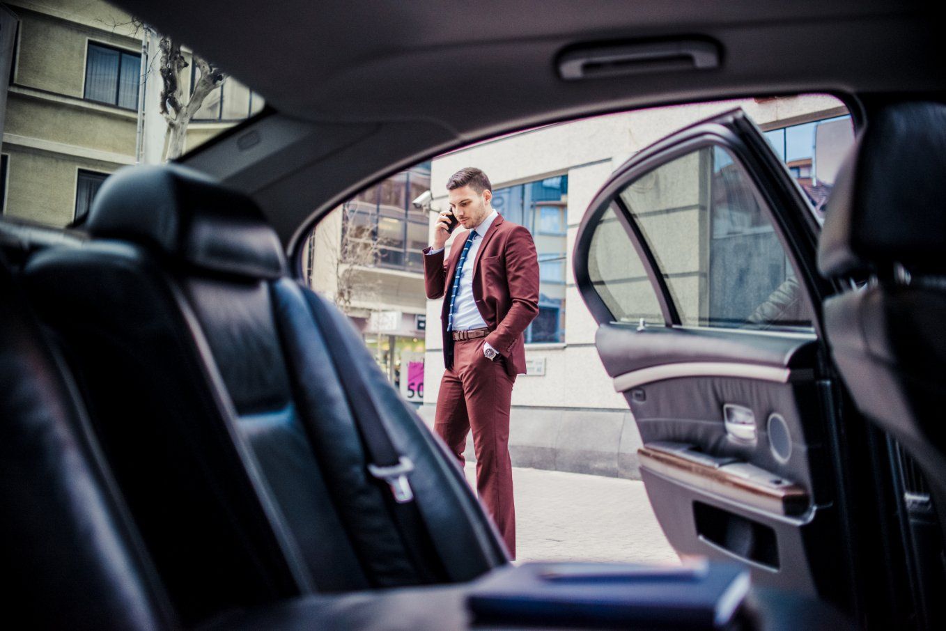 A Man in A Suit Is Talking on A Cell Phone in The Back Seat of A Car — Cachia Upholstery in Tuncurry, NSW
