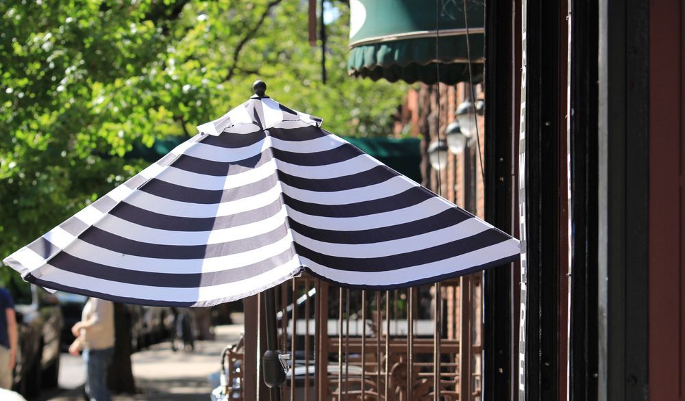 Black-and-white Striped Patio Umbrella Beside a Sidewalk Café — Cachia Upholstery in Taree, NSW