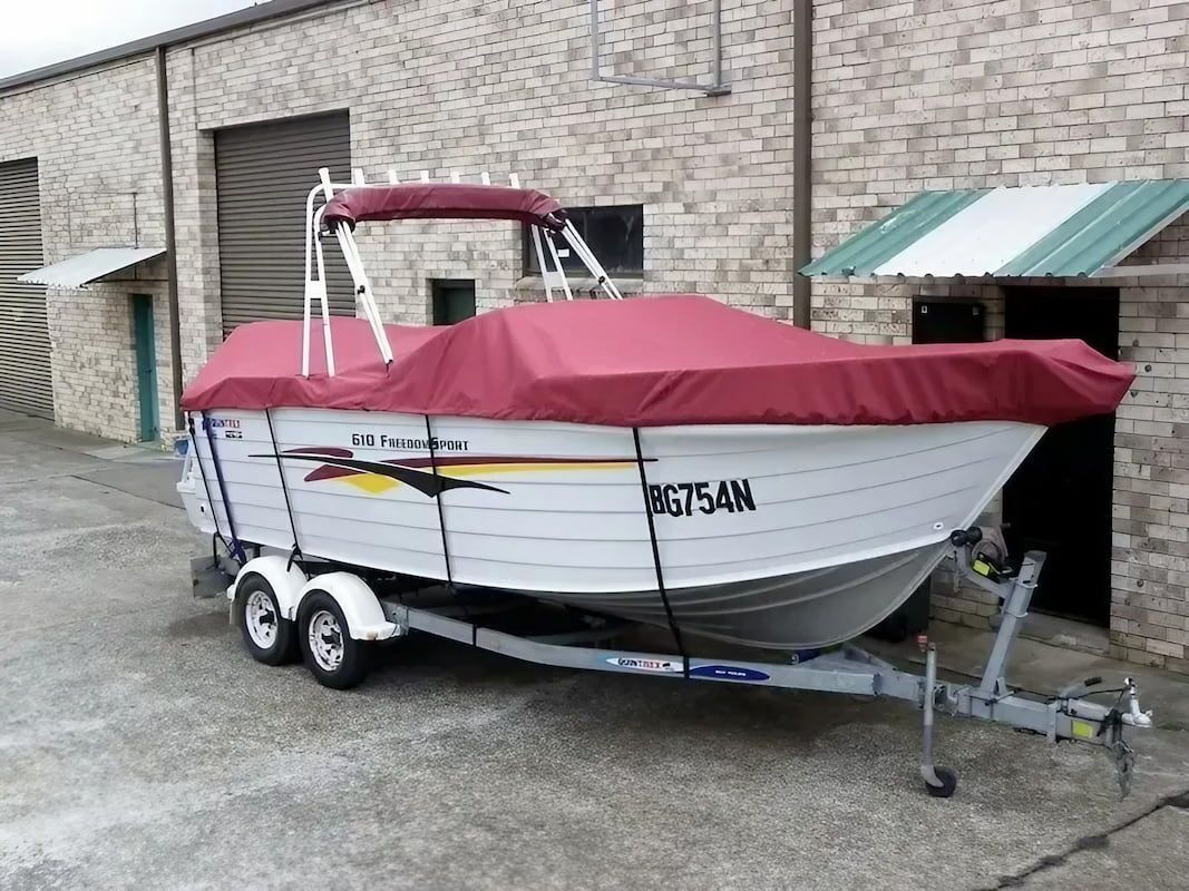 A Boat with A Red Cover on It Is Parked in Front of A Brick Building — Cachia Upholstery in Tuncurry, NSW