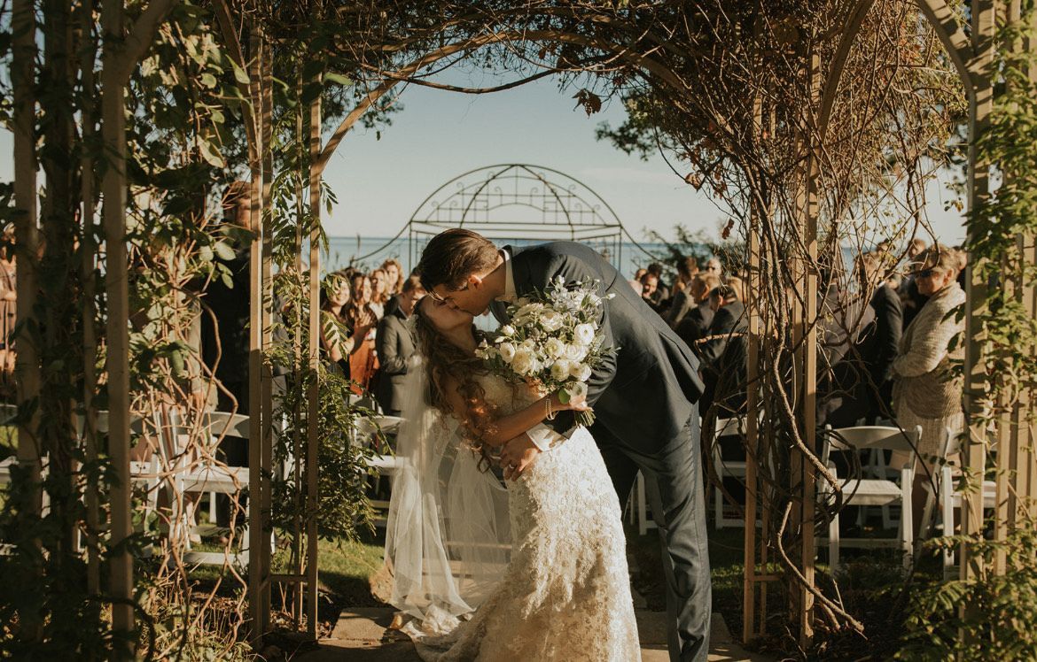 A bride and groom kissing under an arch at their wedding ceremony.