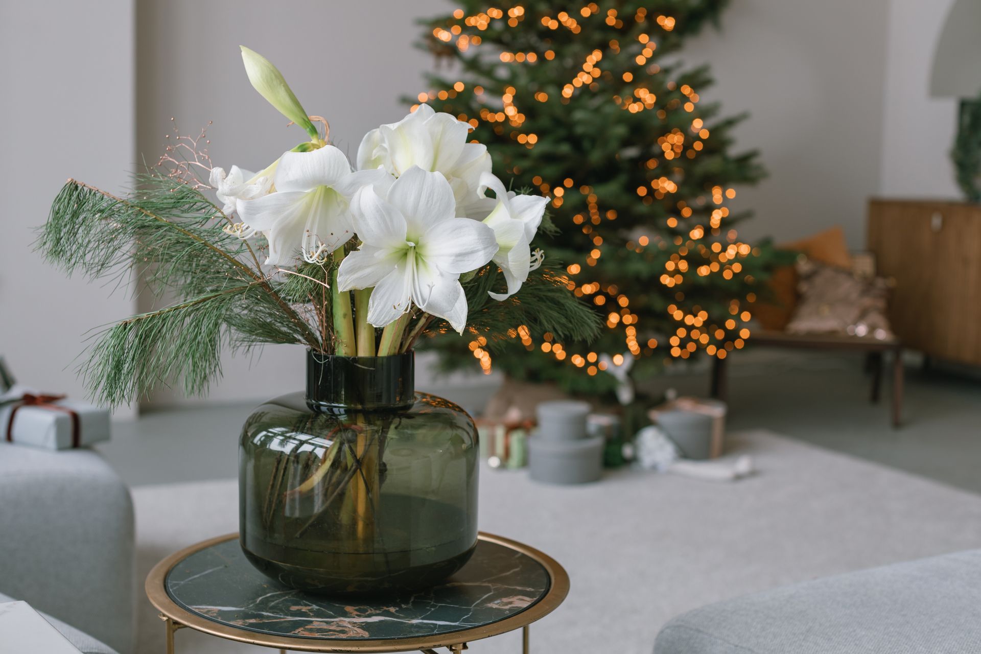 White flowers in a vase on a table, with a Christmas tree and cozy interior in the background.