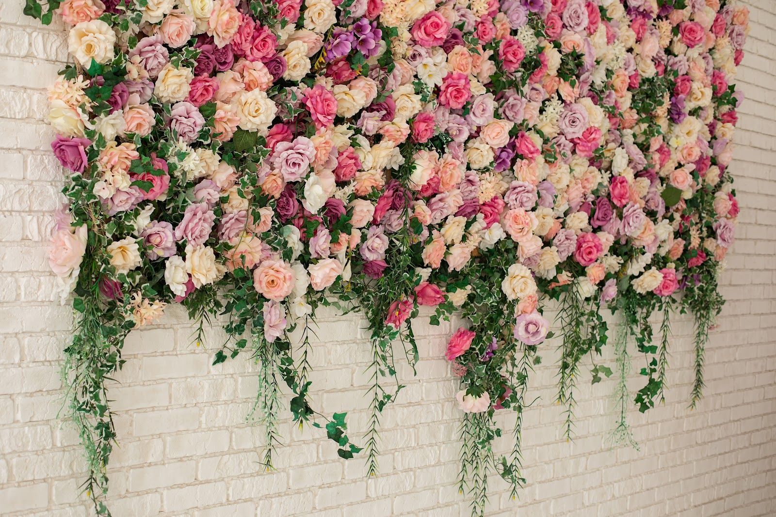 Pink and white floral wall installation on a white brick background with trailing greenery