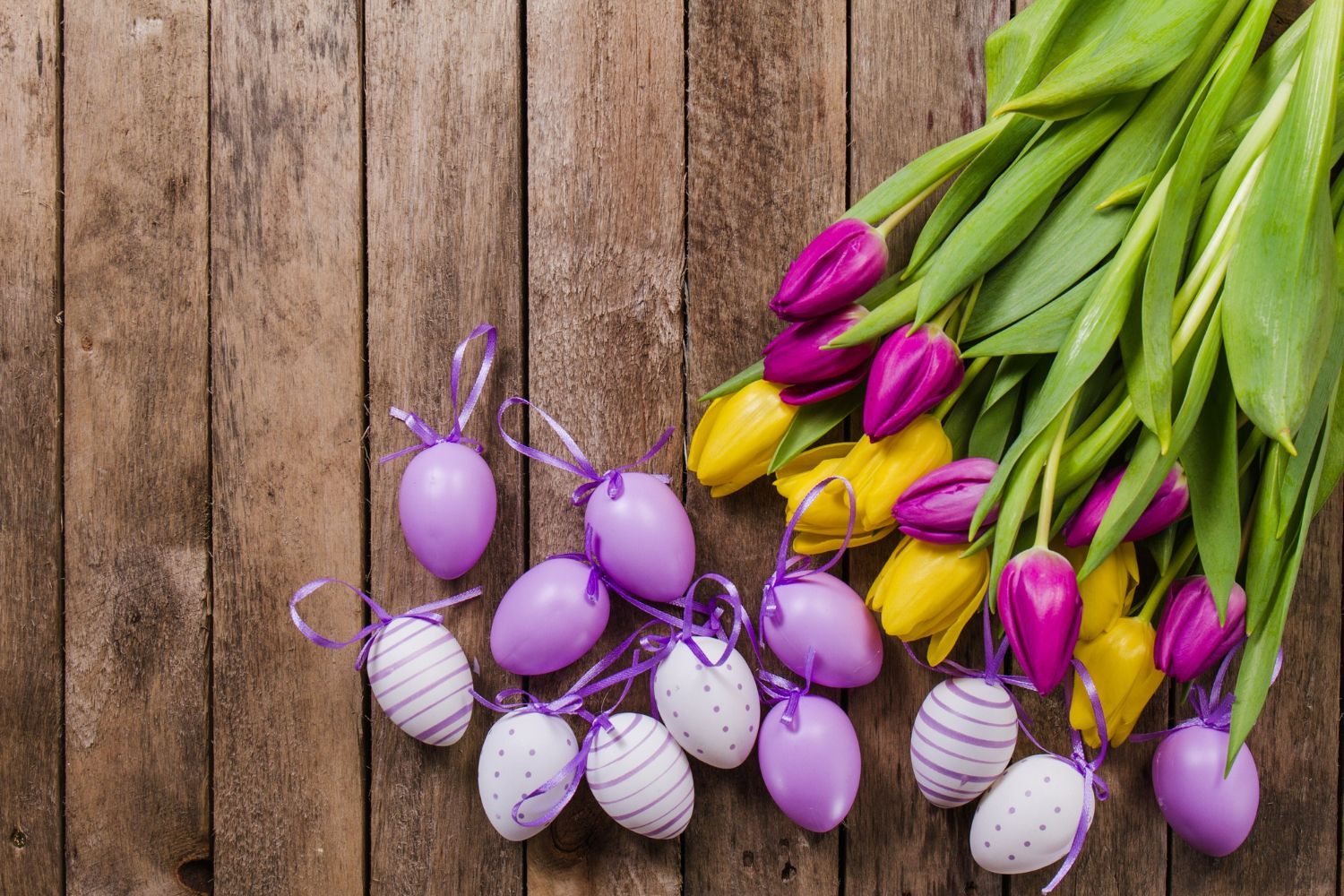 Purple and yellow tulips and easter eggs on a wooden table.