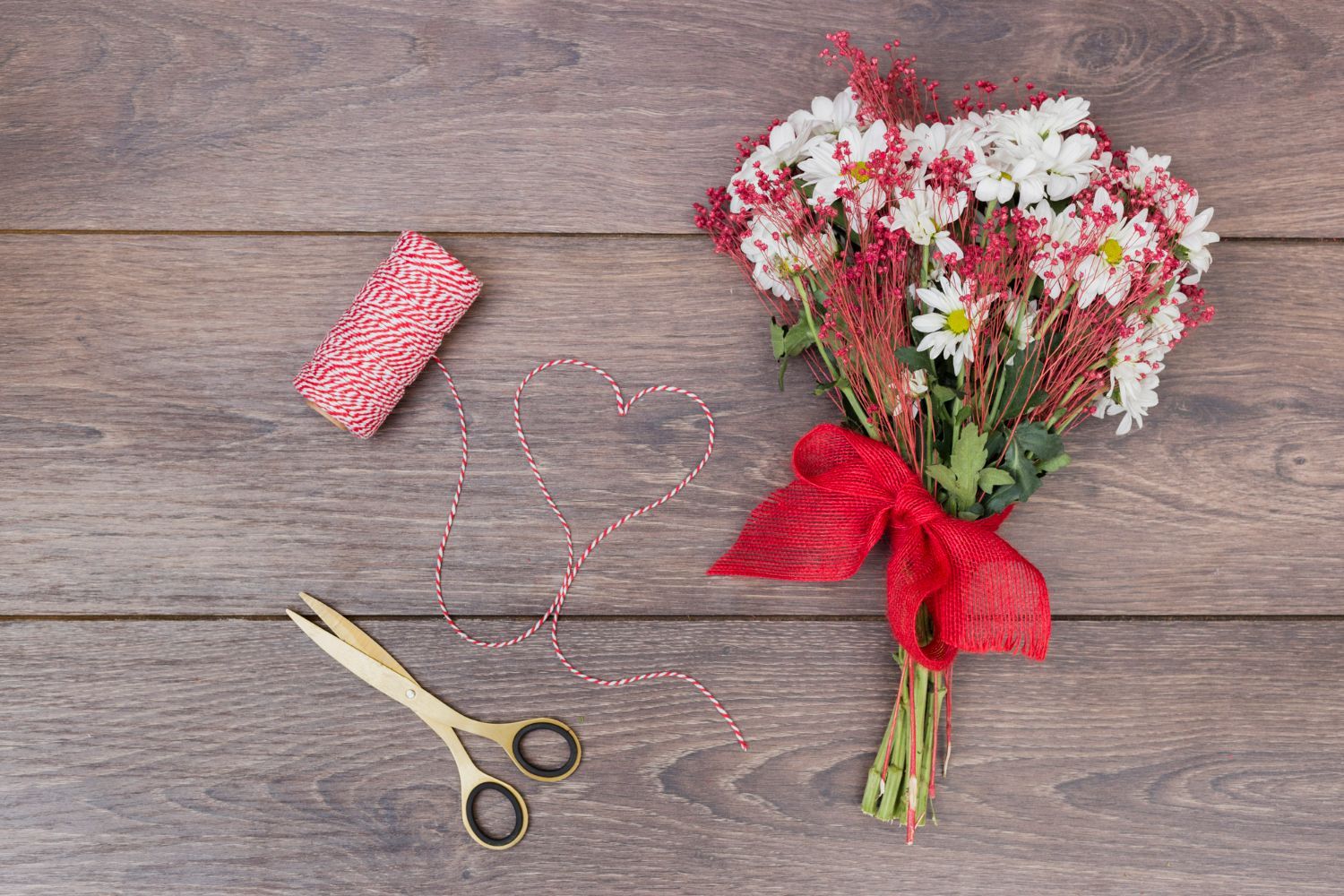 A bouquet of flowers with a red bow and scissors on a wooden table.