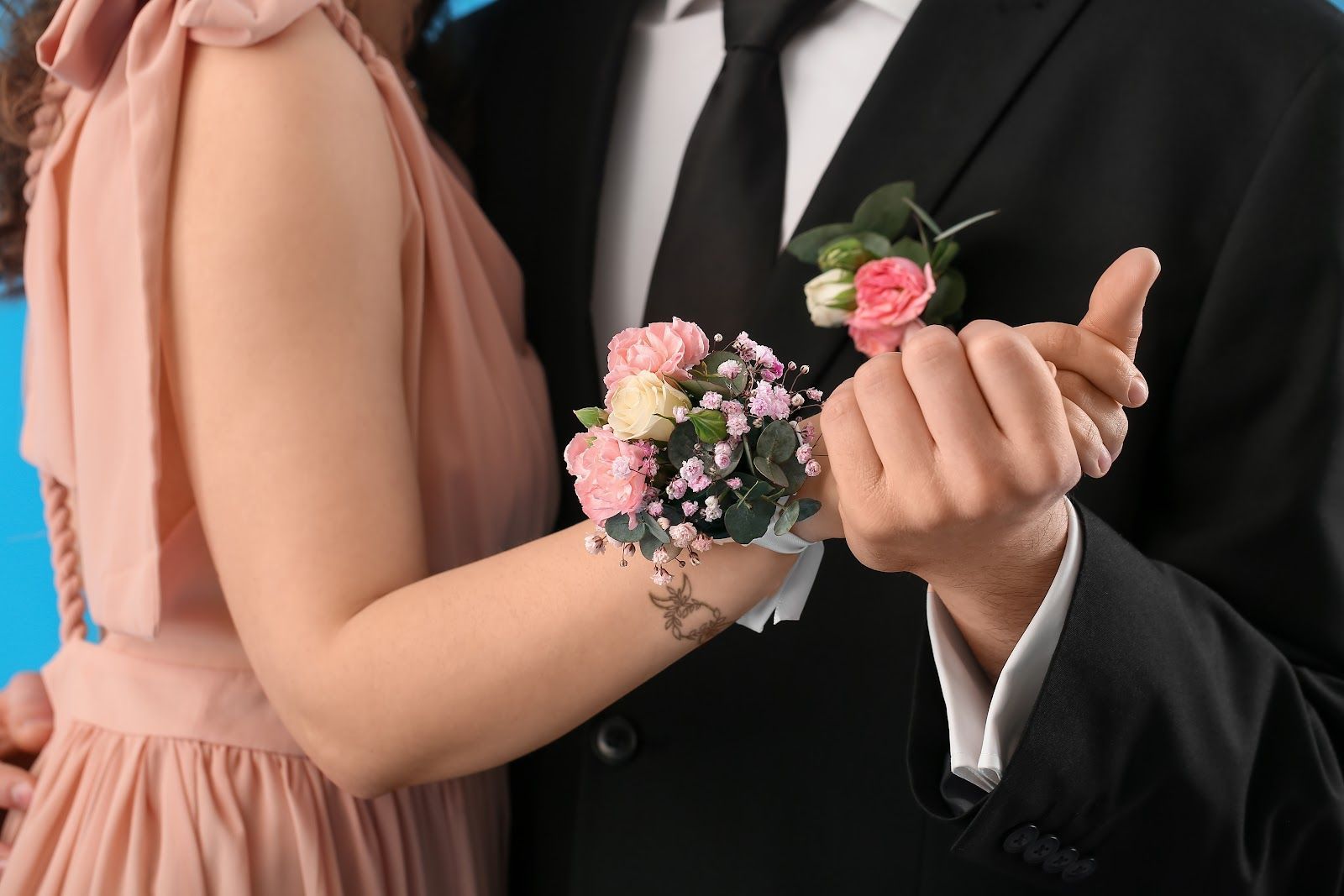 Couple holding hands at a formal event, with a pink floral wrist corsage and black suit