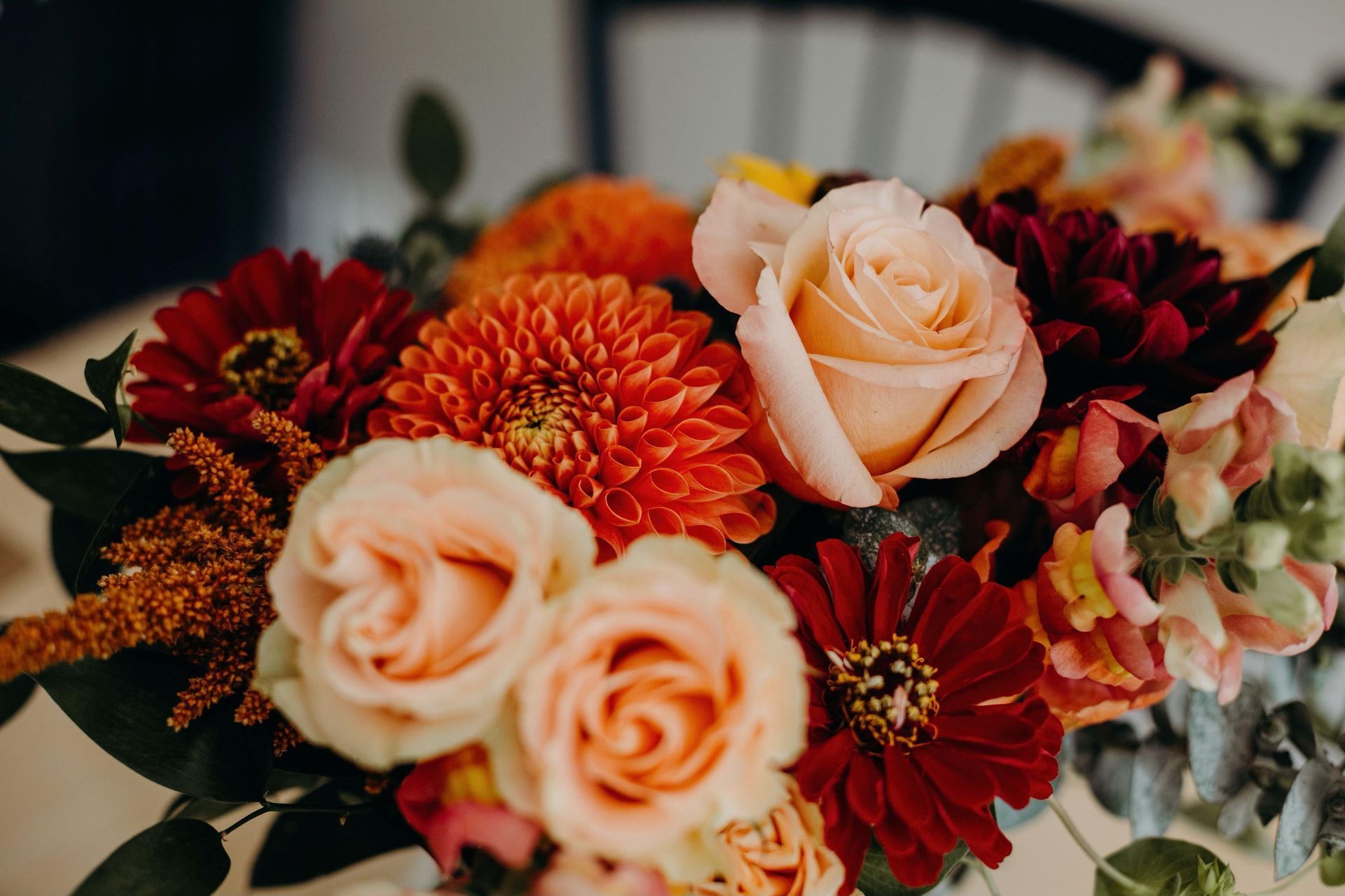 Close-up of a vibrant bouquet with orange dahlias, peach roses, and burgundy zinnias.
