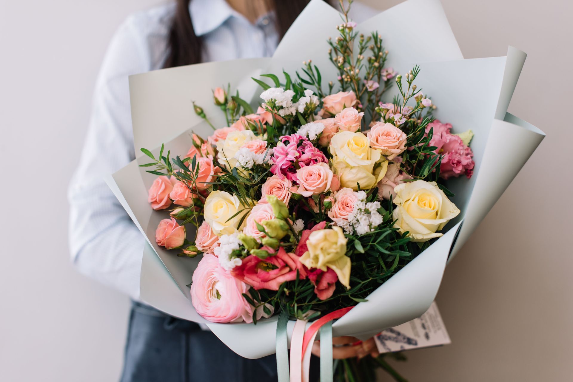 Woman holding a colorful bouquet of pink, yellow, and white flowers wrapped in light blue paper.