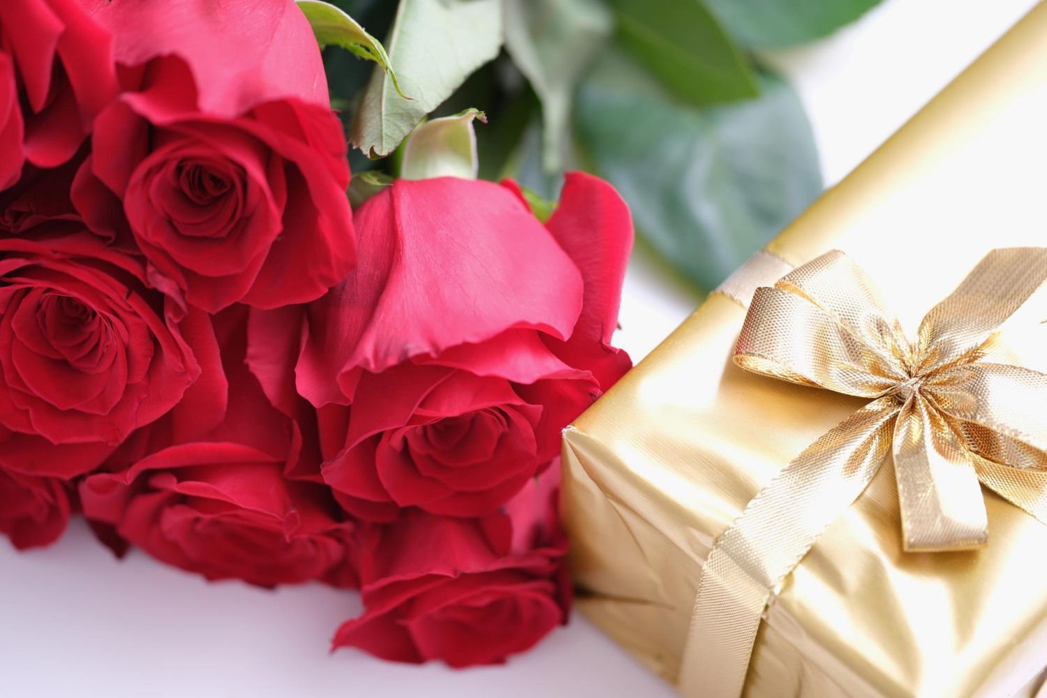 A bouquet of red roses next to a gold gift box