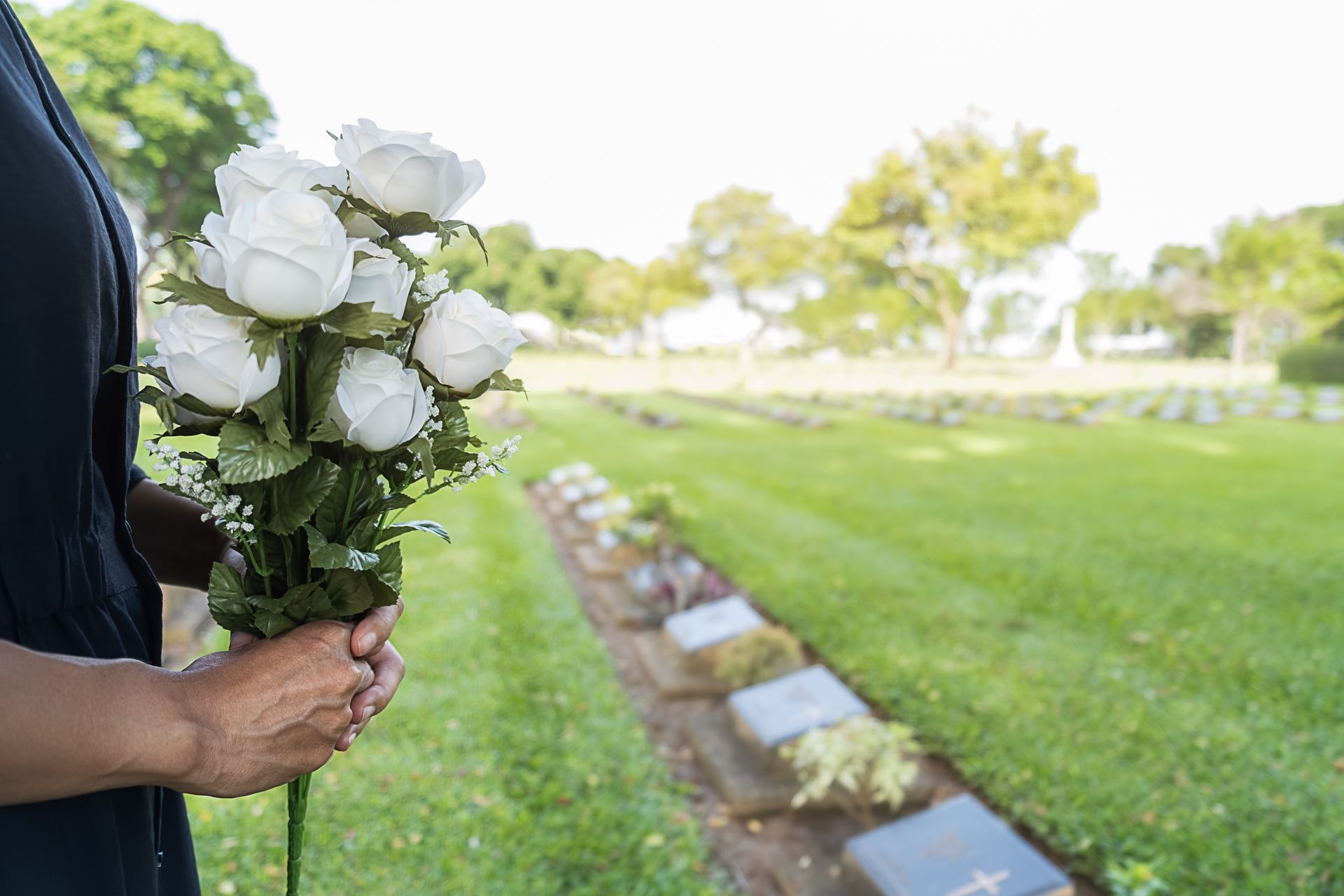 A woman is holding a bouquet of white roses in a cemetery.