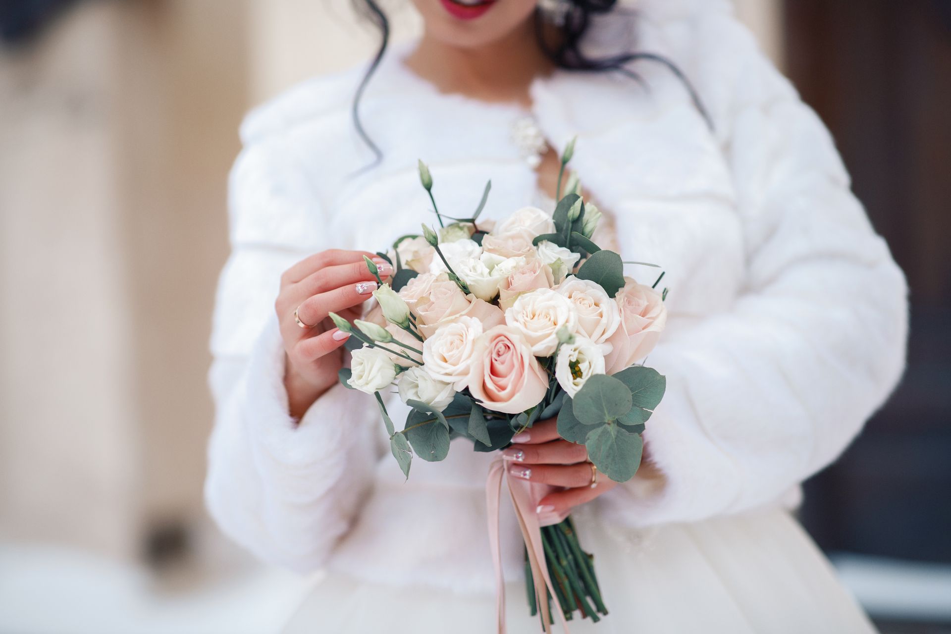 Bride in white fur coat holding a bouquet of pink and white roses.