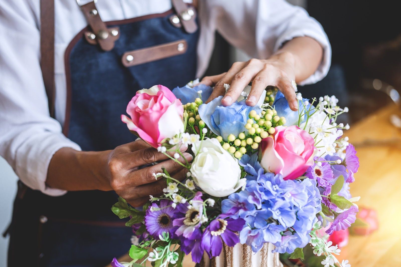 Florist arranging a bouquet of pink, blue, purple, and white flowers in a vase